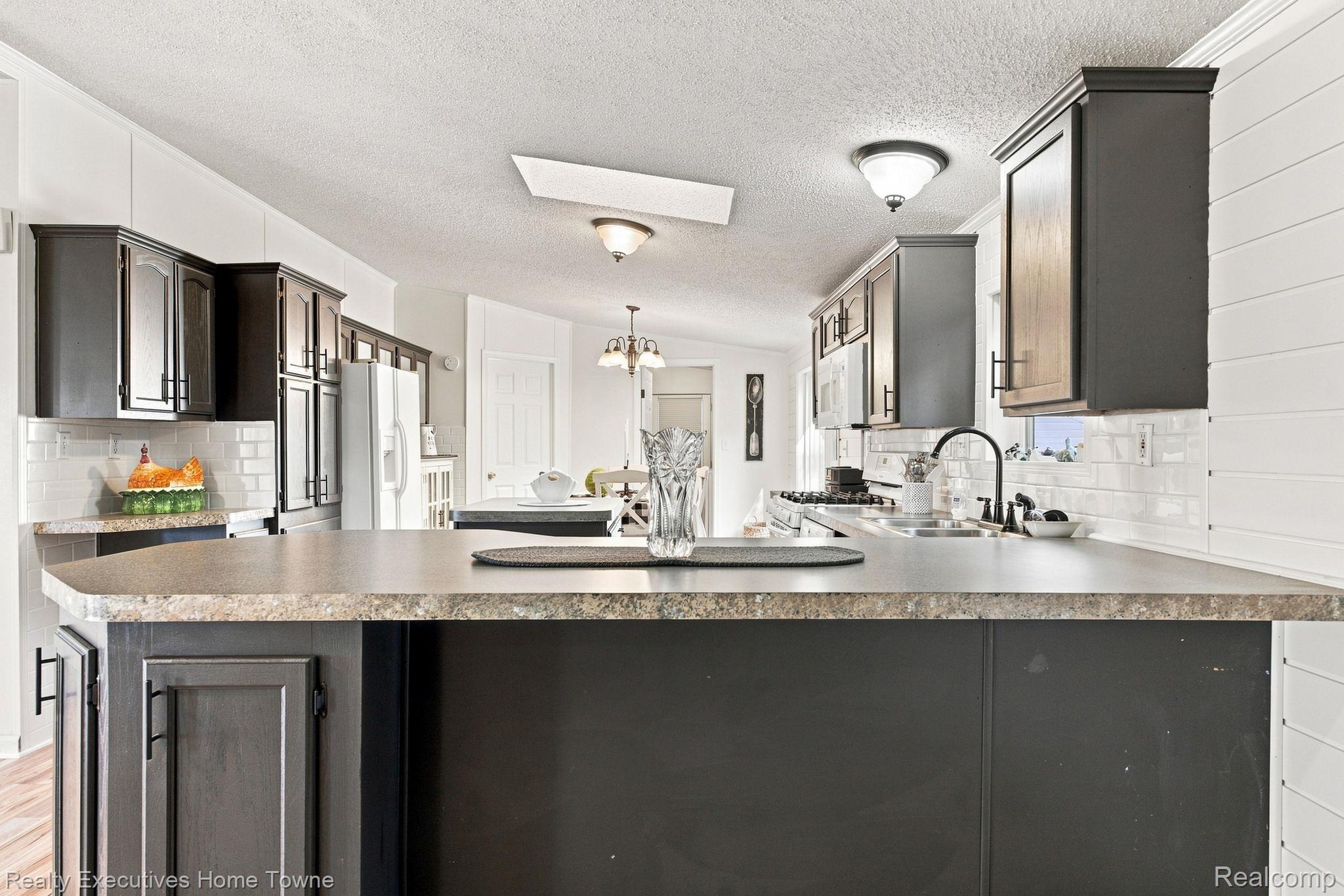 Bright kitchen with a broad dark island, granite countertop, dark cabinetry, and white tile backsplash.