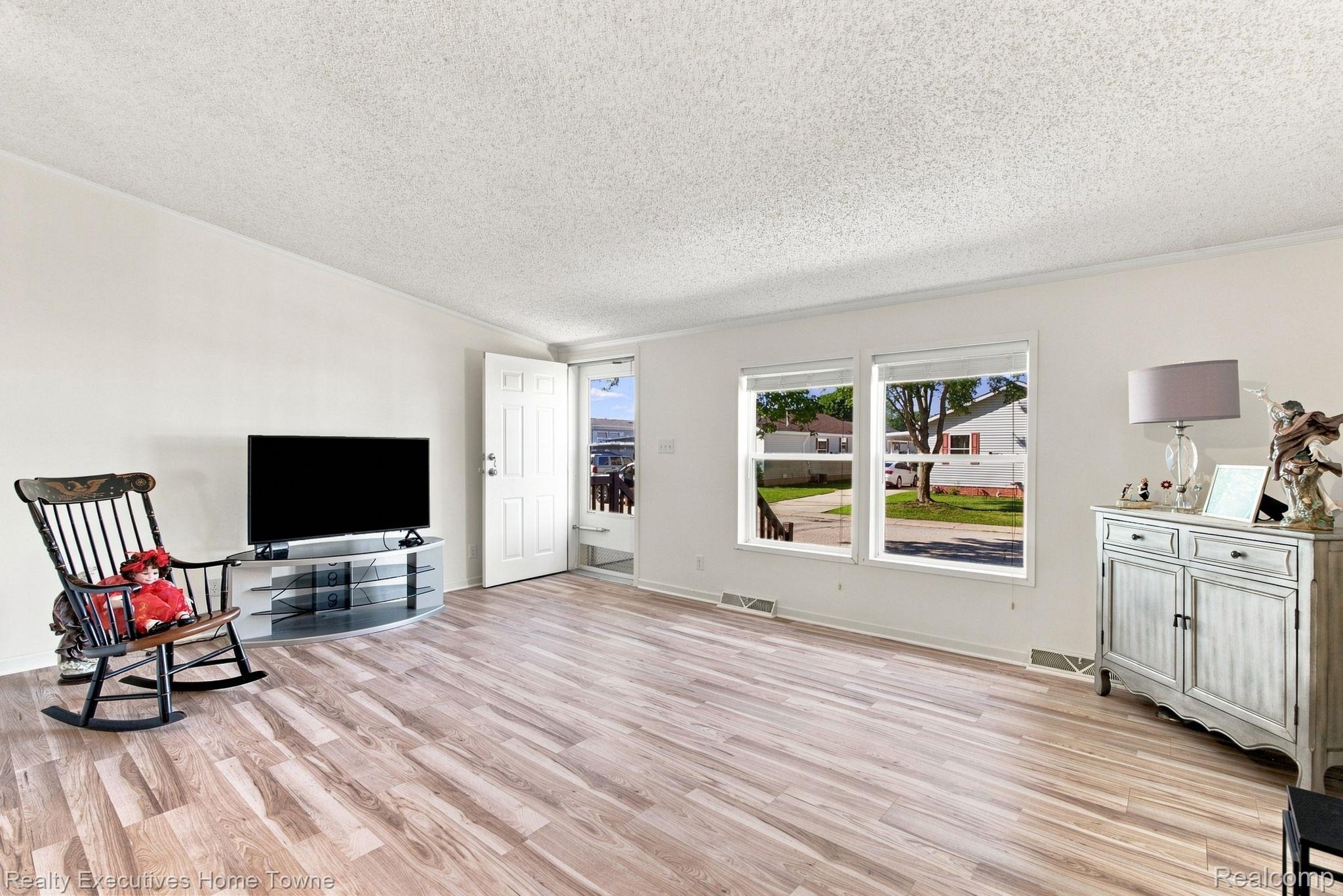 Living room with light wood-look flooring, rocking chair, and large street-facing windows.