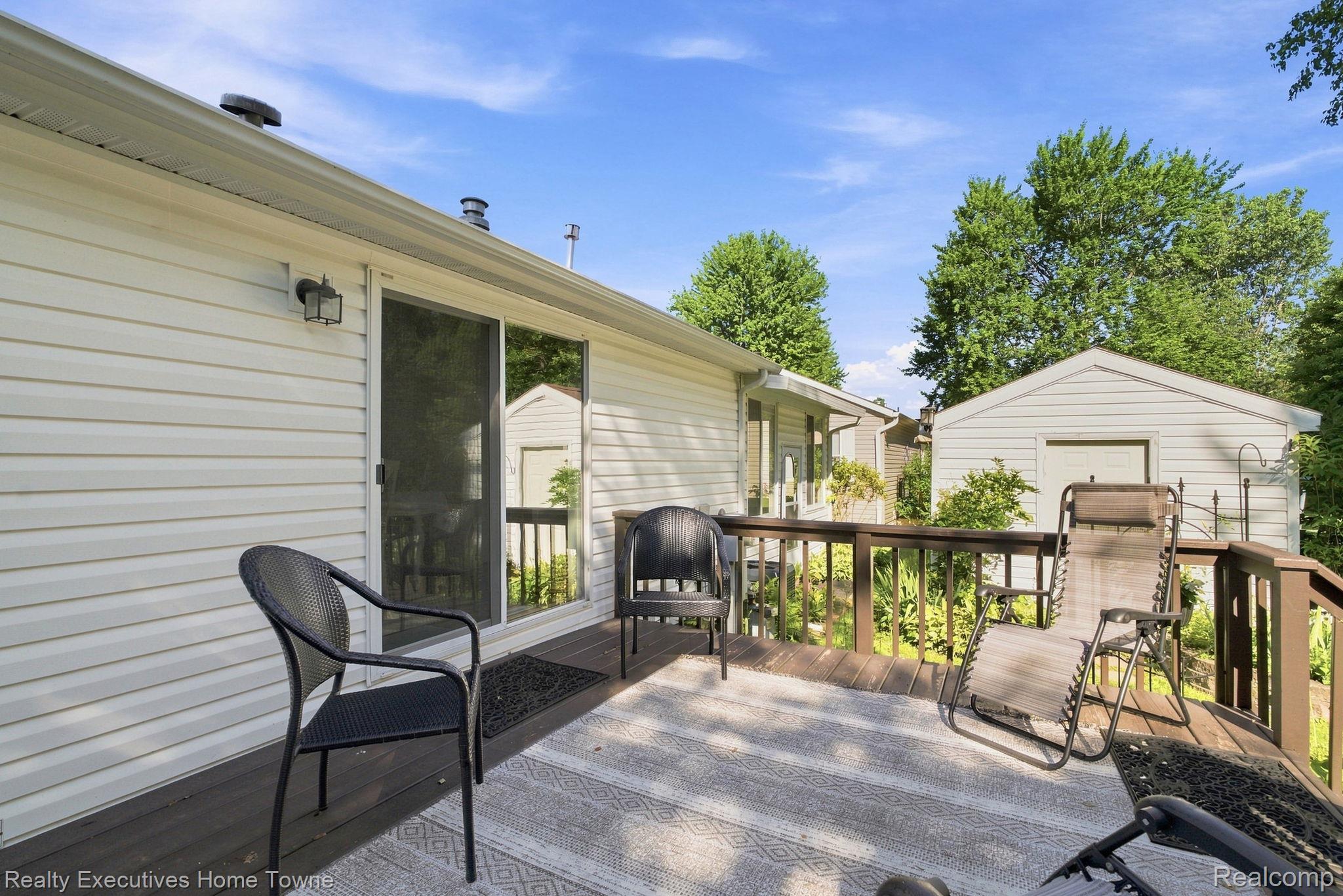 Furnished wooden deck beside a white-sided home, with outdoor seating and a detached garage.