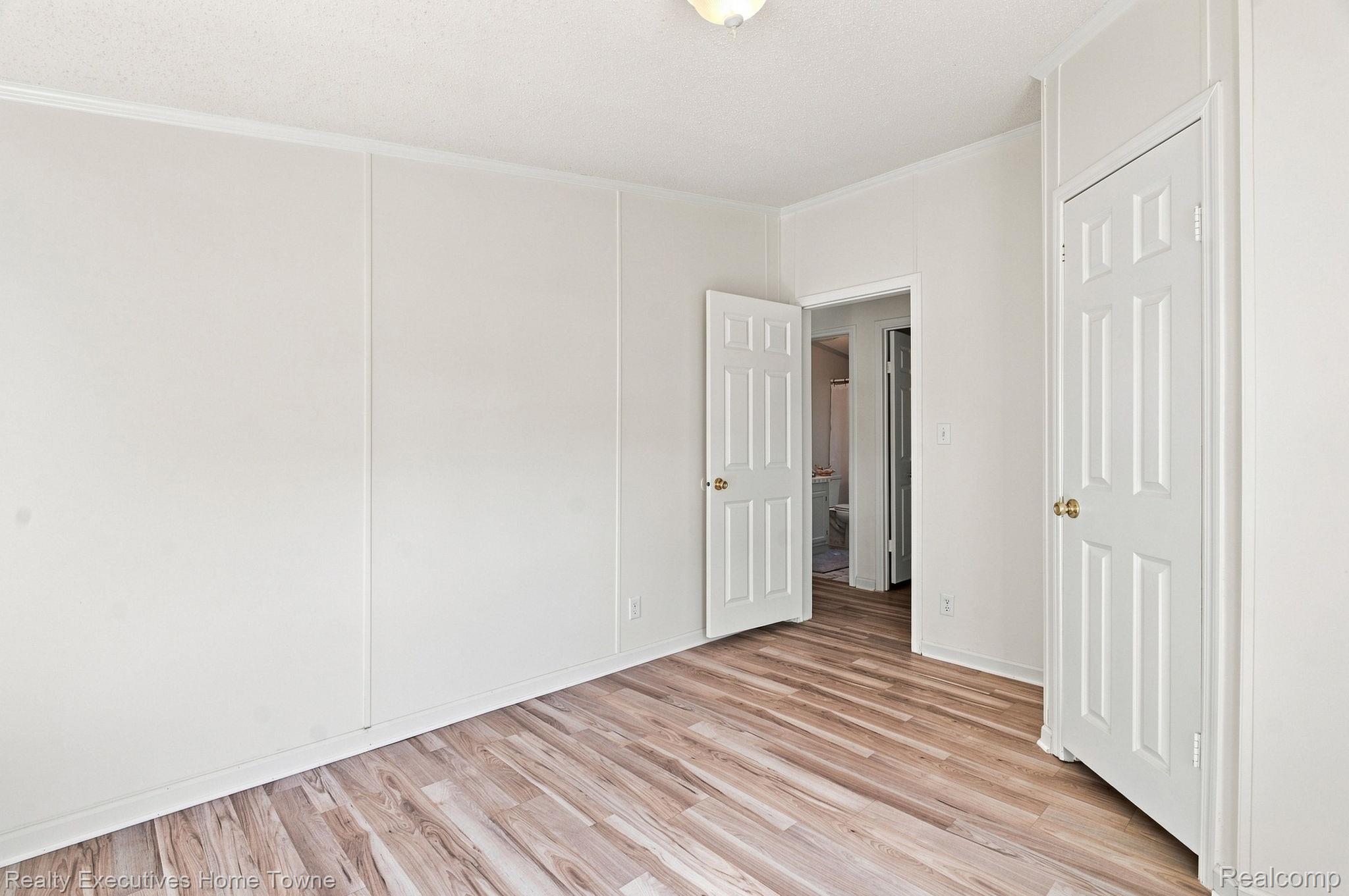 Empty room with wood-look flooring and open doors to a bathroom and hallway.