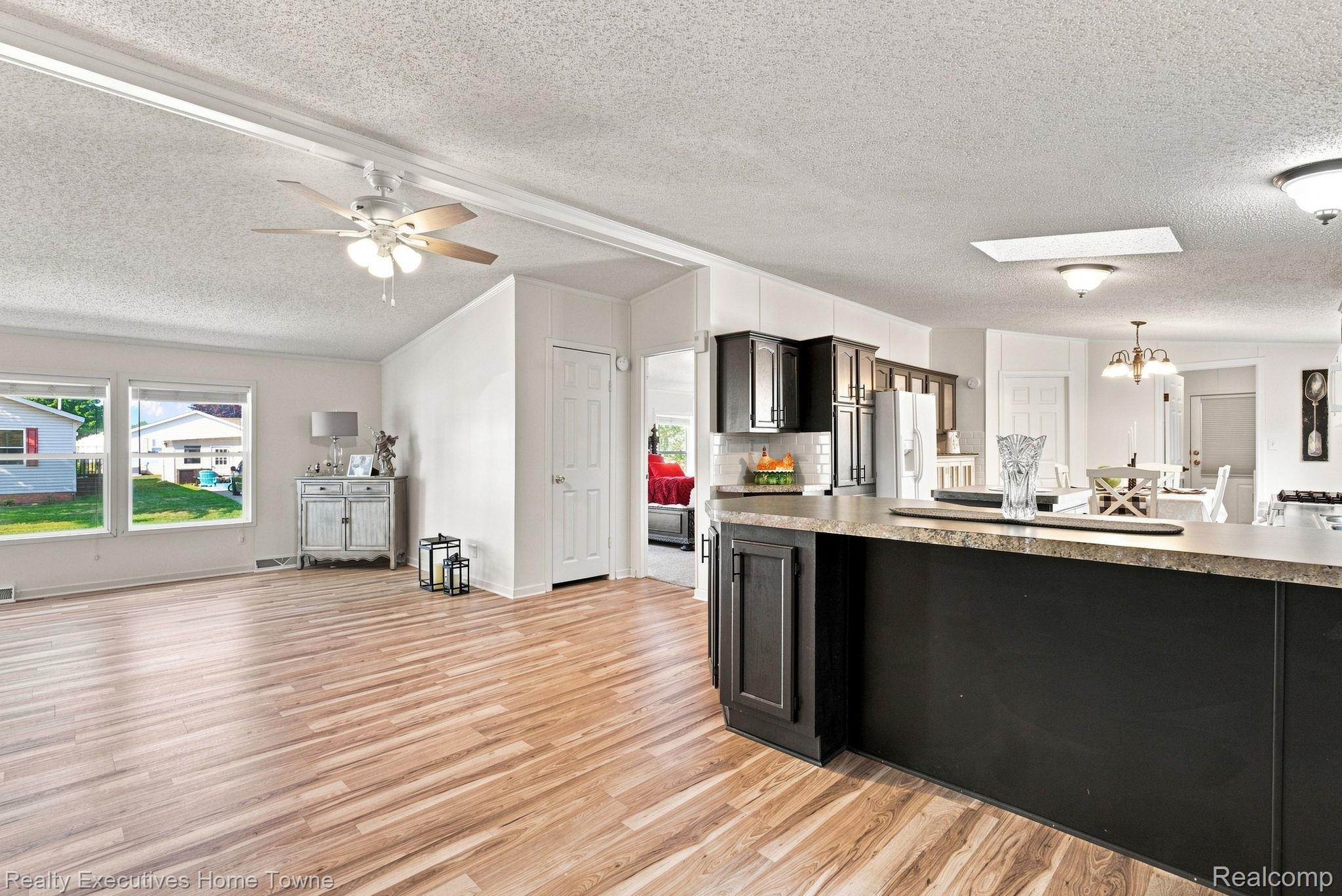 Open-plan kitchen with dark cabinets, a large island, stainless appliances, and light wood flooring.