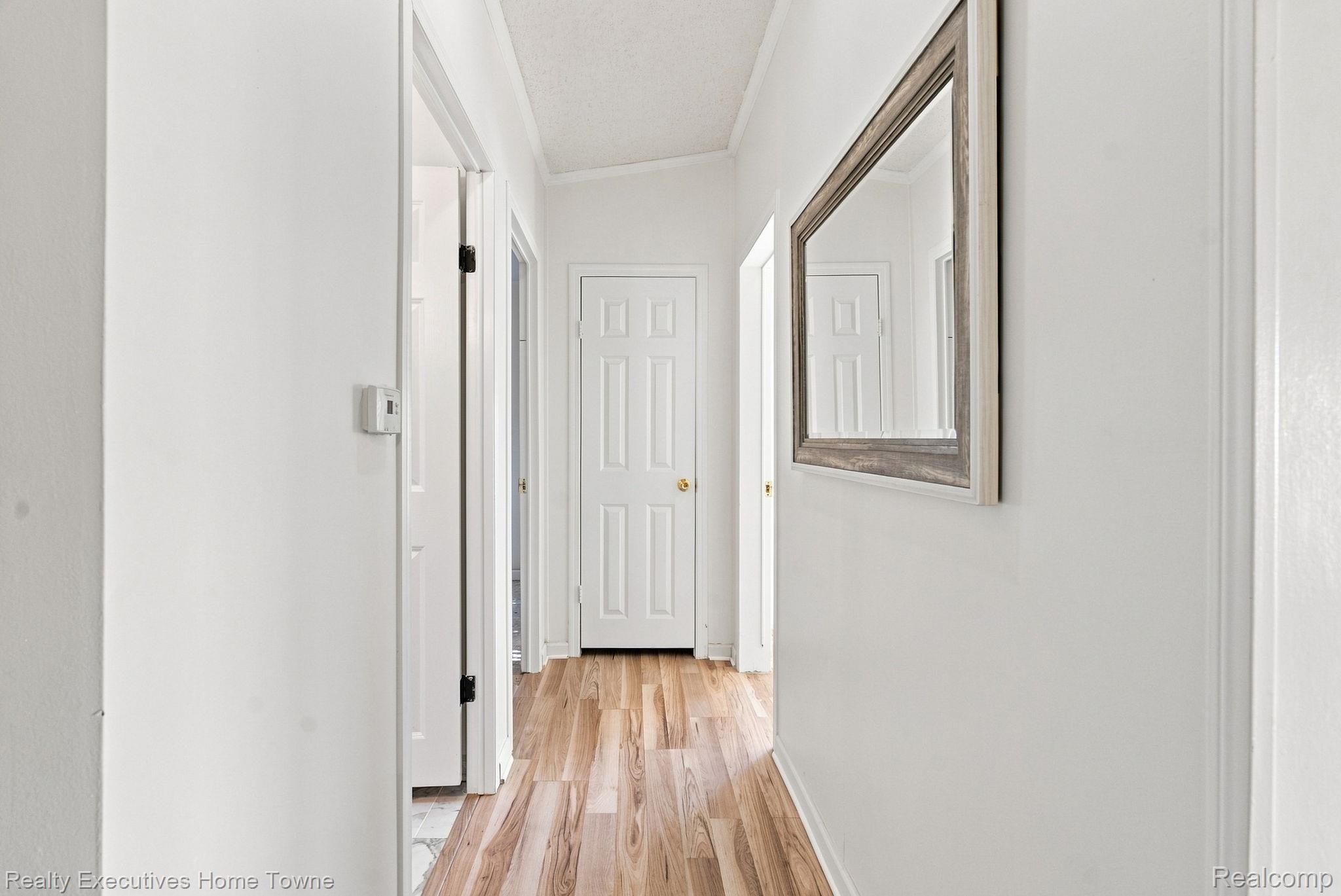 Bright hallway with light wood flooring, white doors, and a large framed mirror.