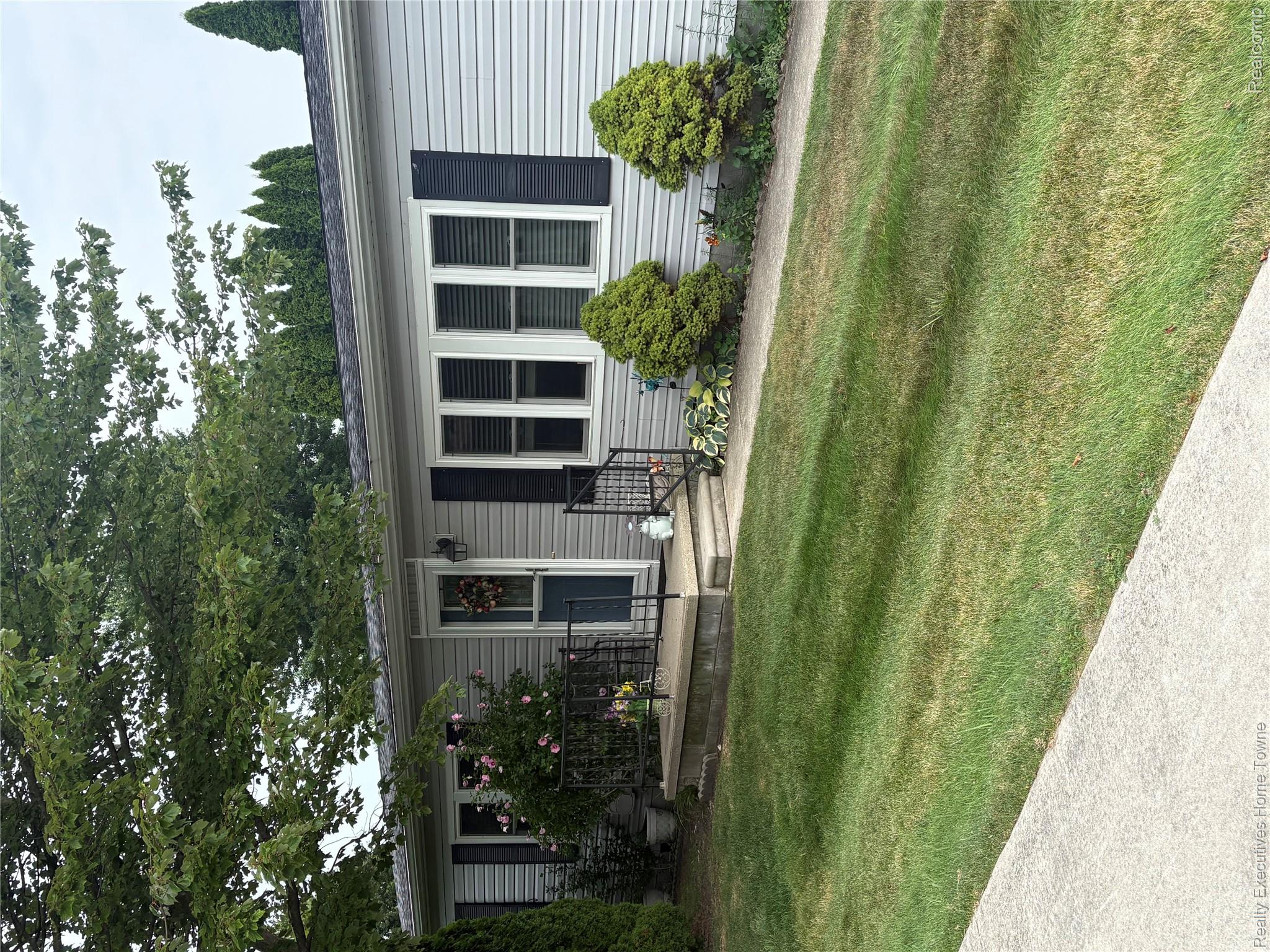 Single-story gray-sided home with dark shutters, a small raised porch, and landscaped front lawn.