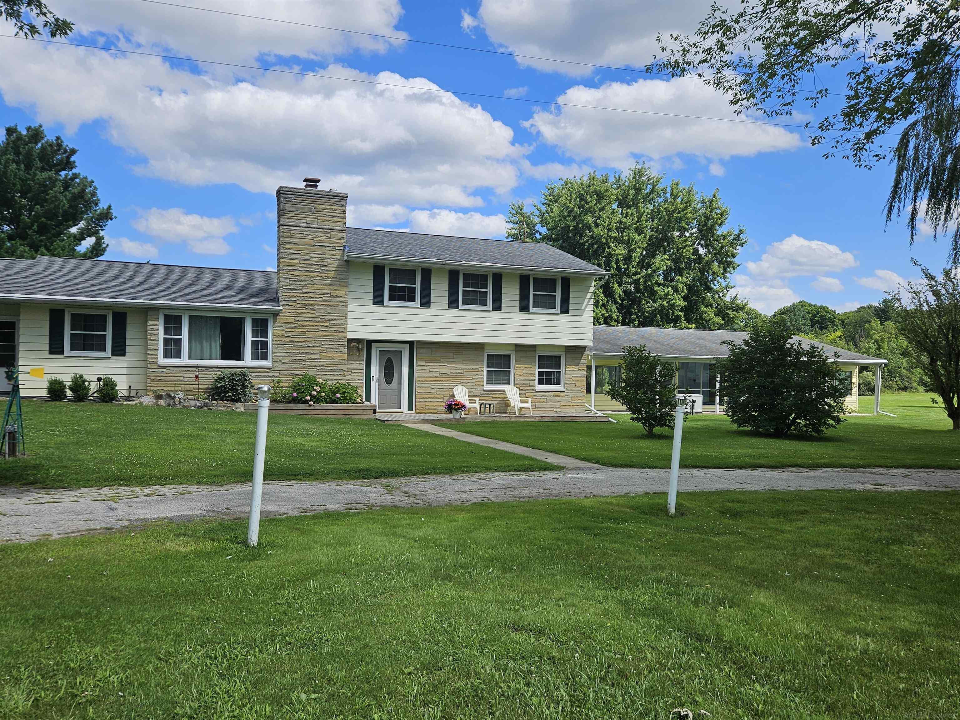 Two-story house with a tall stone chimney, broad lawn, and covered patio.