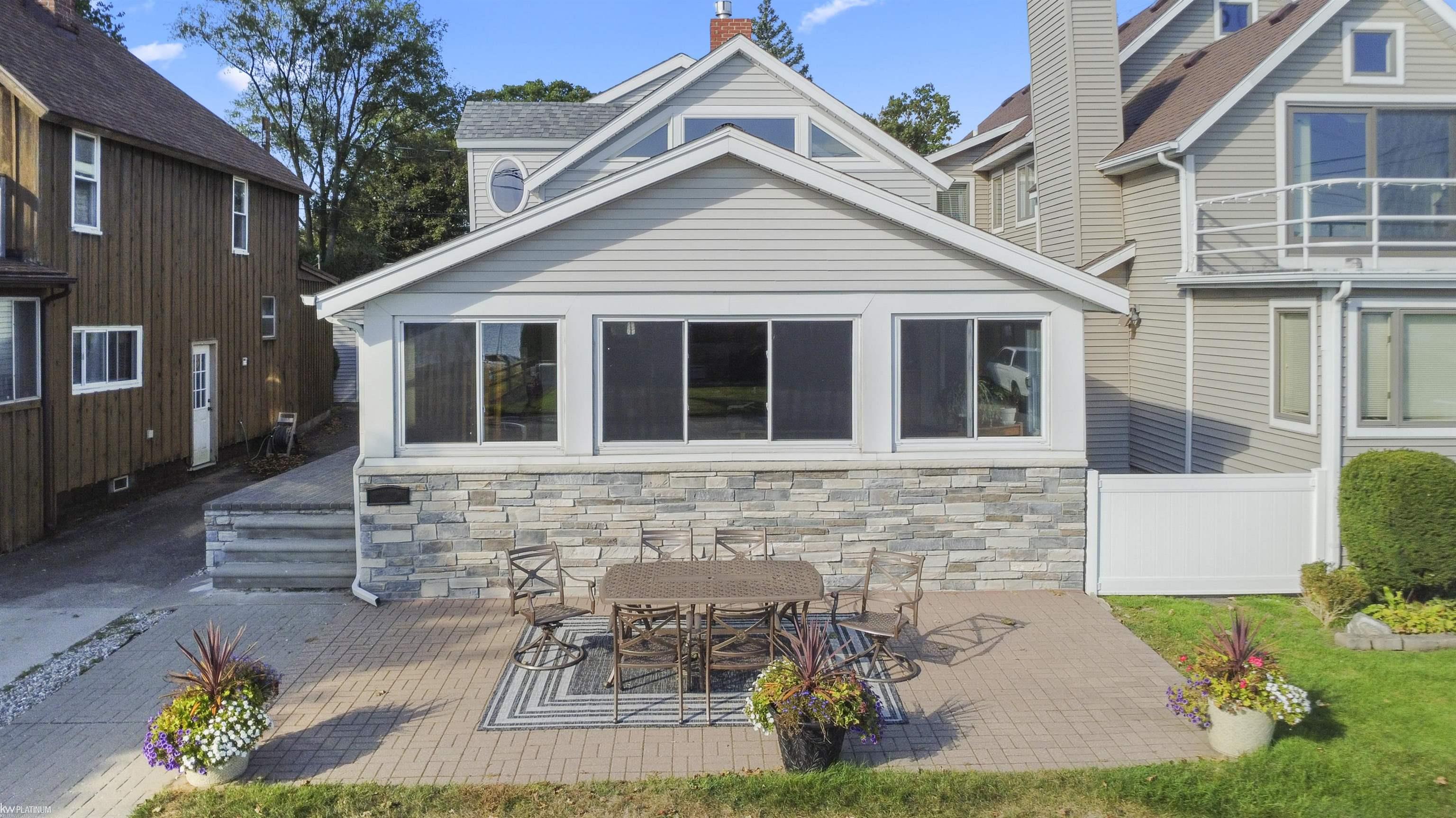 House rear with stone foundation and a furnished brick patio with colorful flower planters.