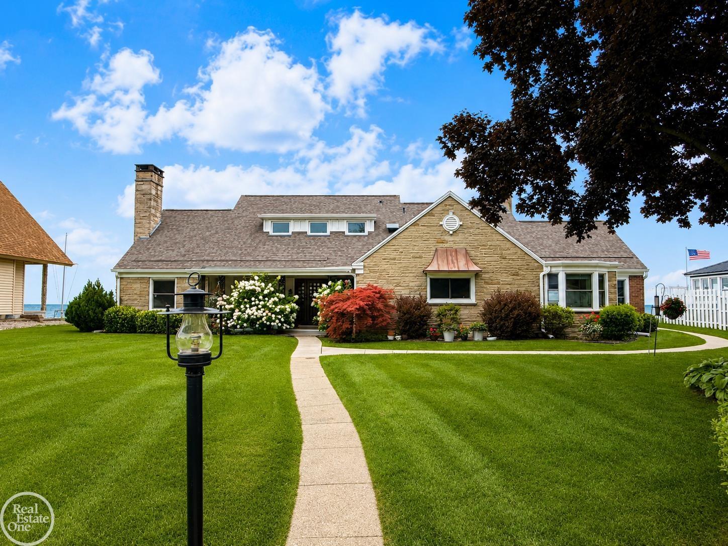Stone house with a landscaped lawn and walkway, water visible beside the property.