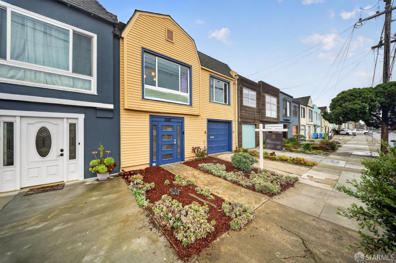 Yellow two-story home with blue trim, a blue garage, and a landscaped front yard.