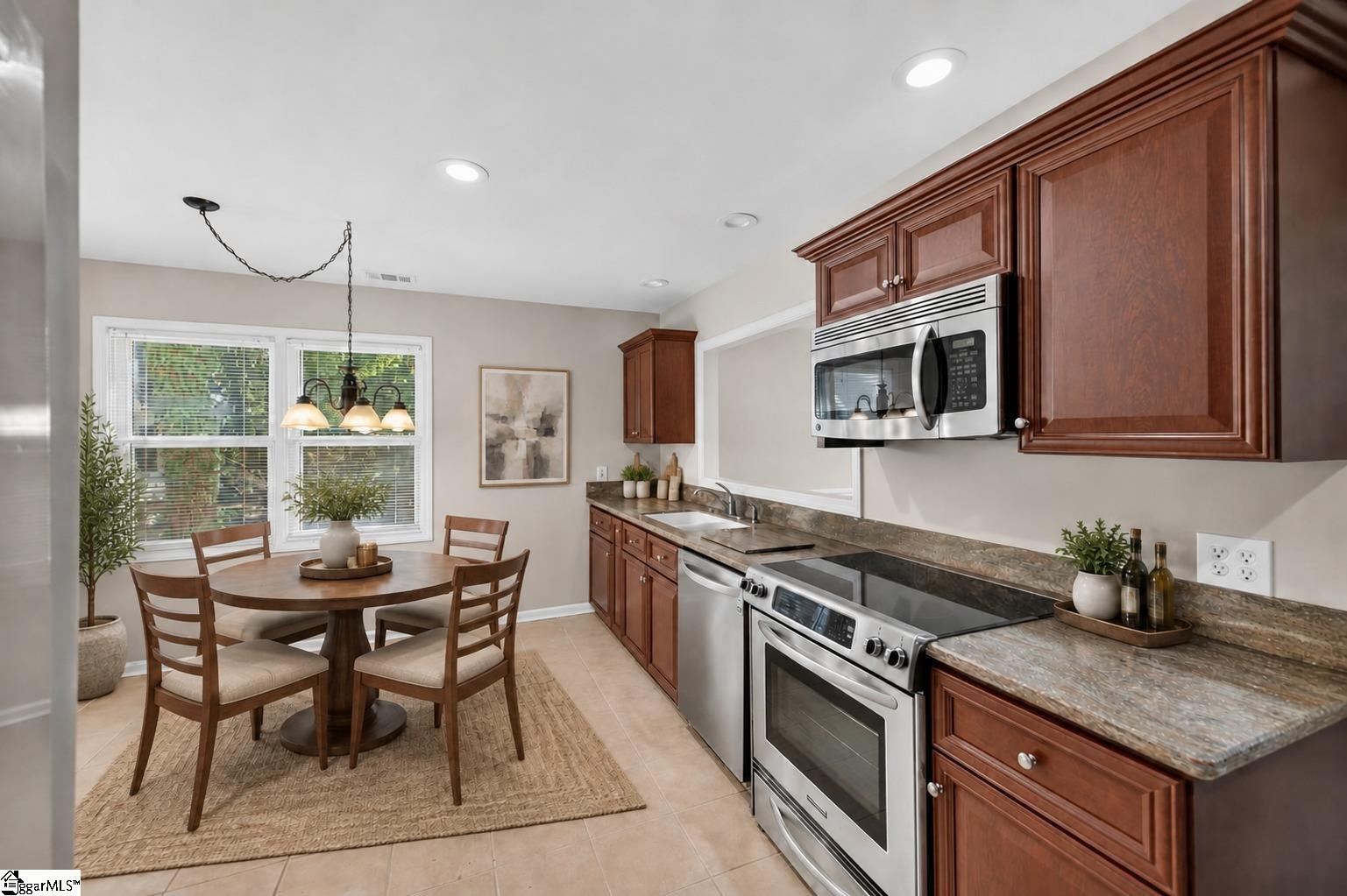 Kitchen with reddish-brown cabinets, granite counters, stainless steel appliances, and a round dining table by the windows.