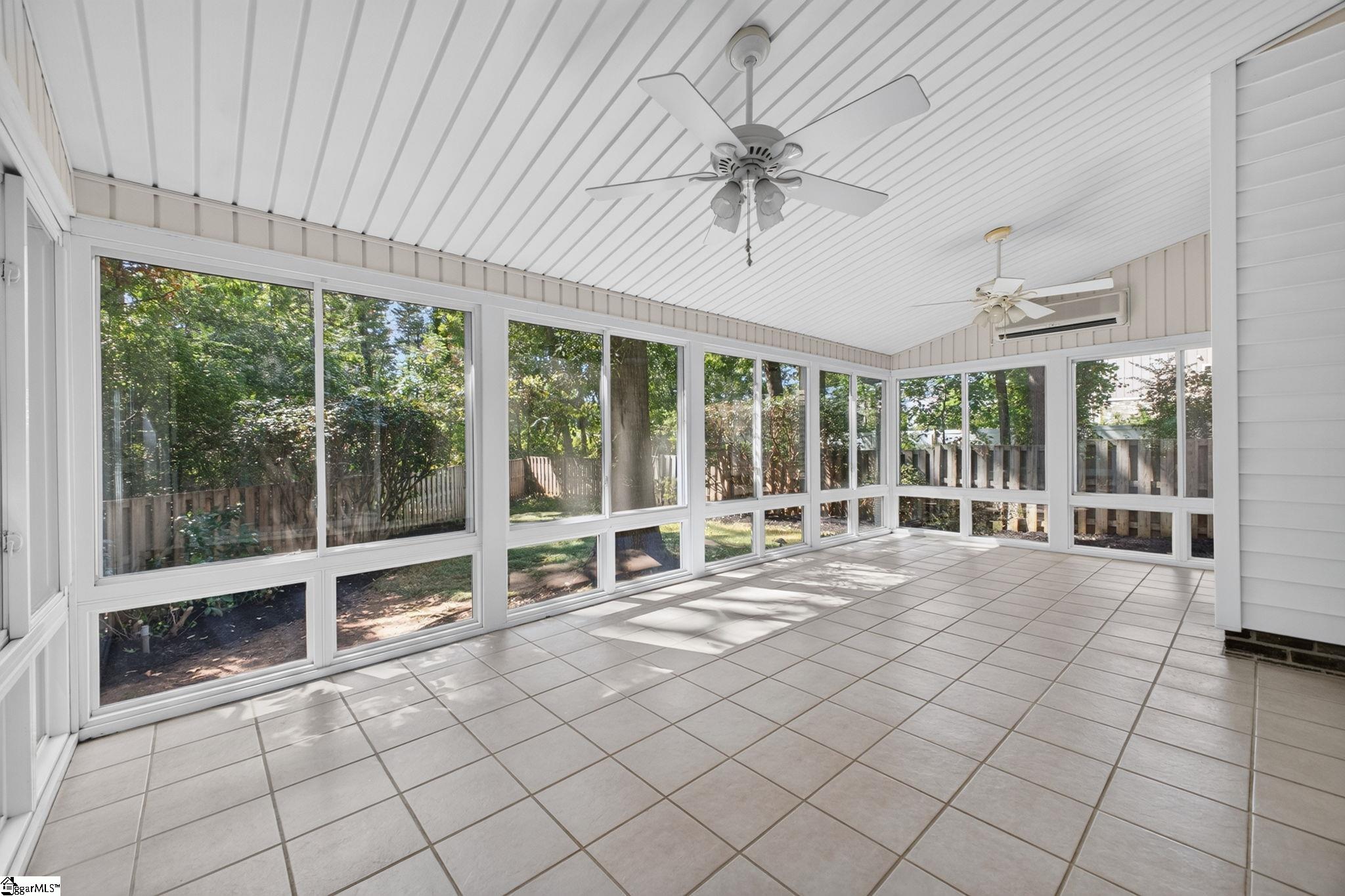 Enclosed sunroom with wraparound windows, tiled floor, and two ceiling fans.
