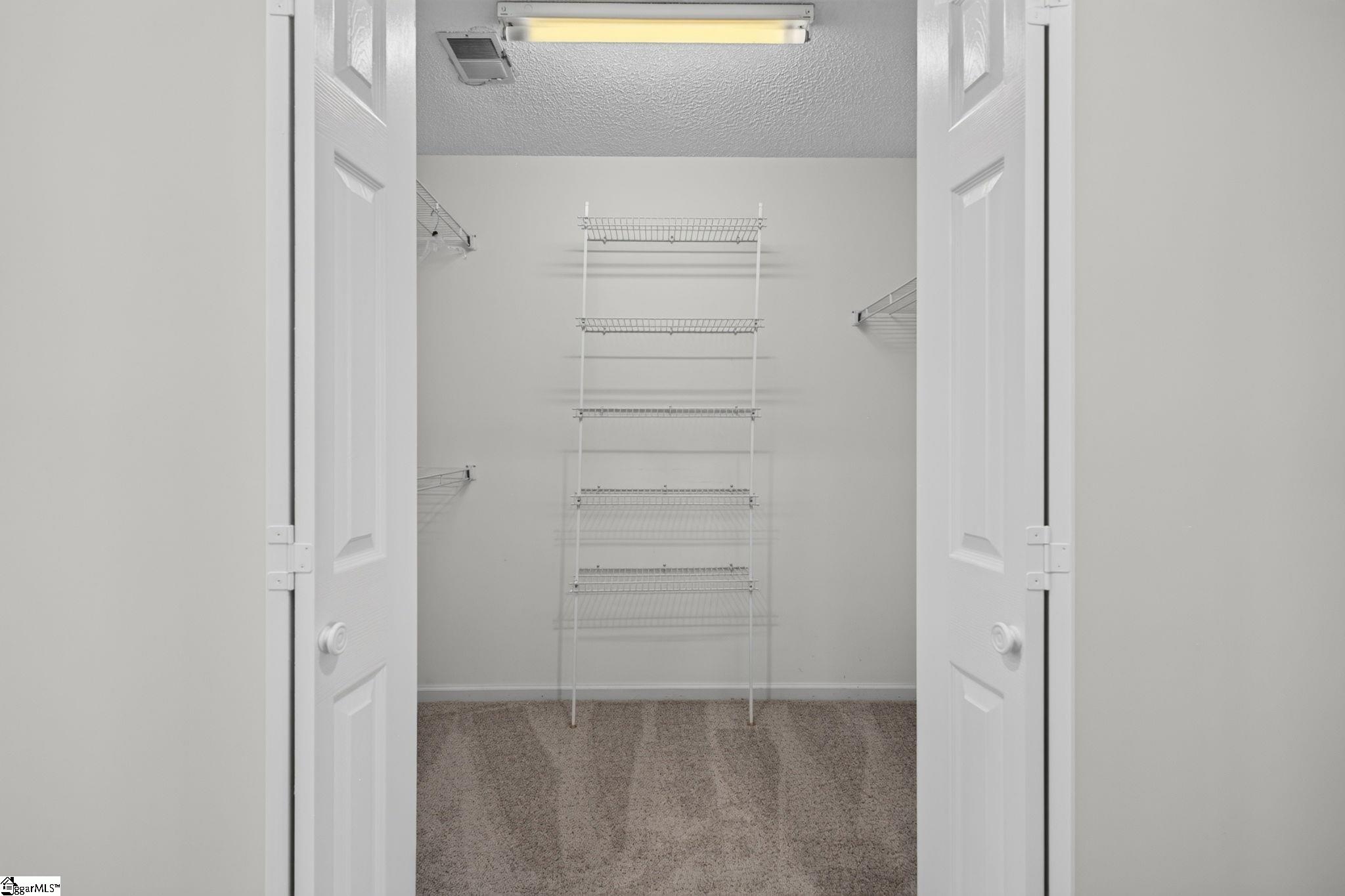 Empty walk-in closet with white wire shelving, beige carpet, and open double doors.