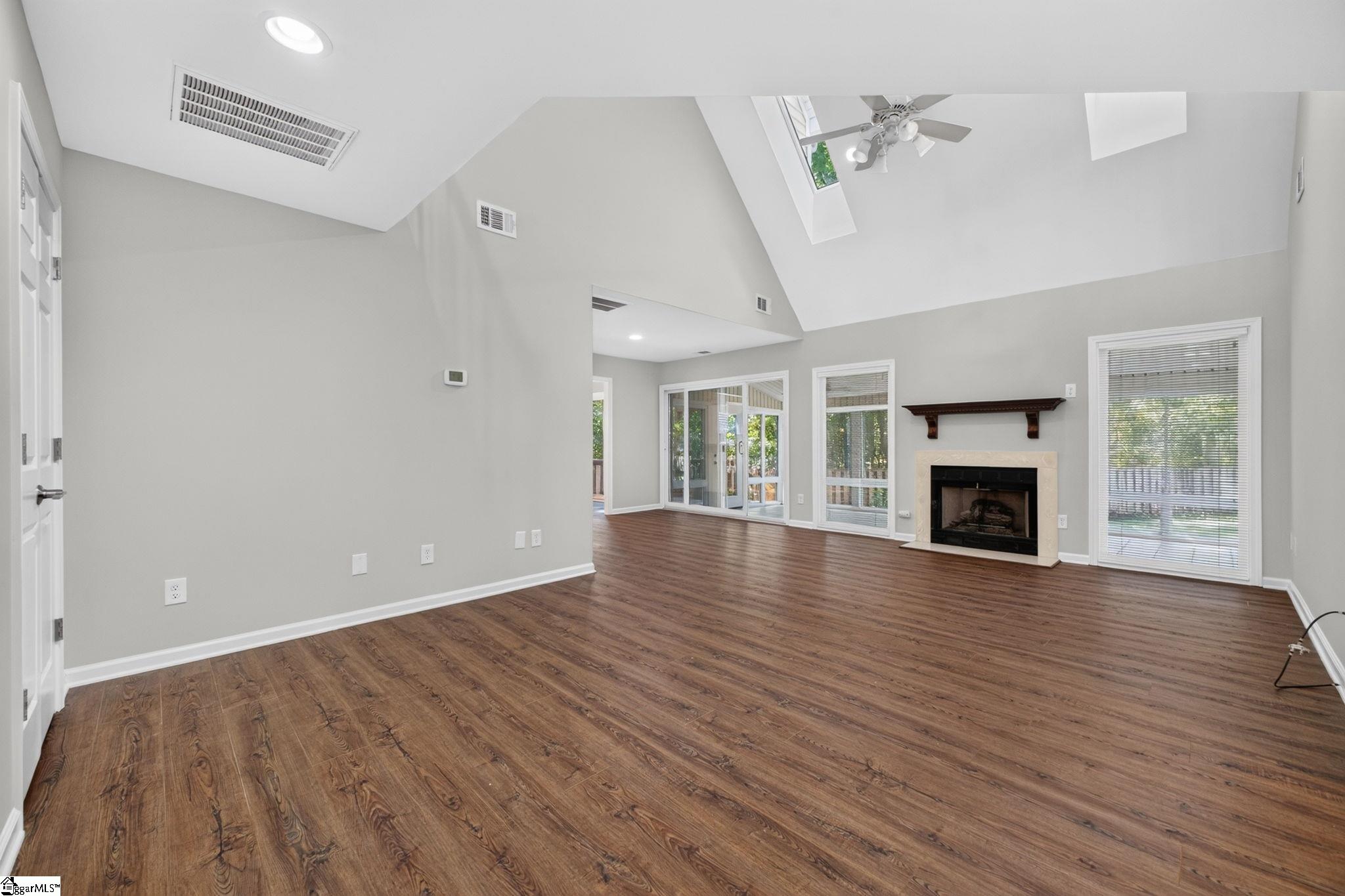 Vacant living room with a vaulted skylit ceiling, wood floors, and a fireplace.