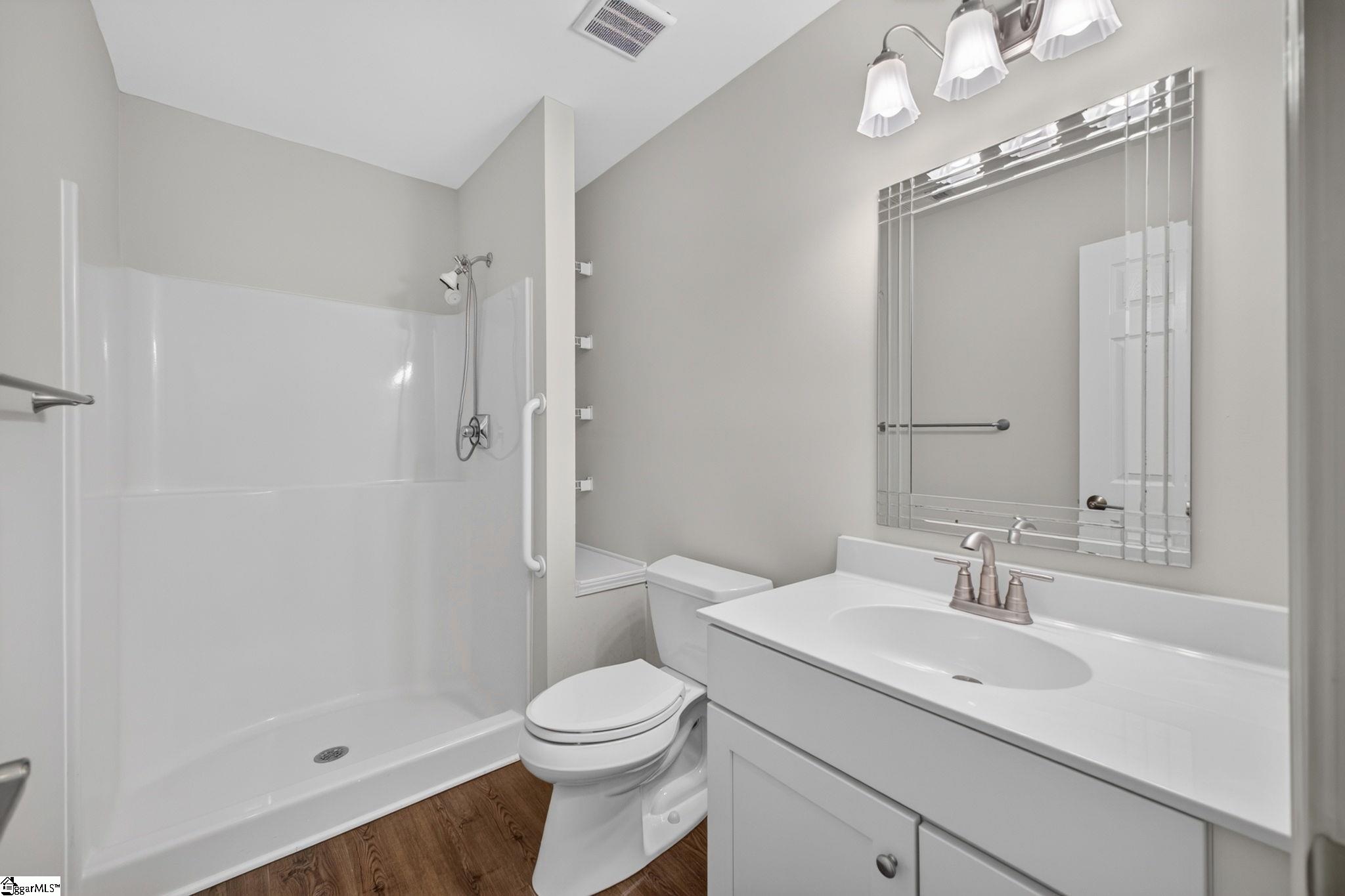 Bathroom with a white walk-in shower, toilet, and vanity with a large framed mirror.
