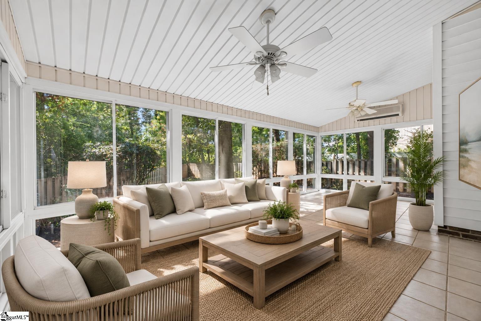 Furnished sunroom with broad windows, wicker seating, and views of leafy trees.