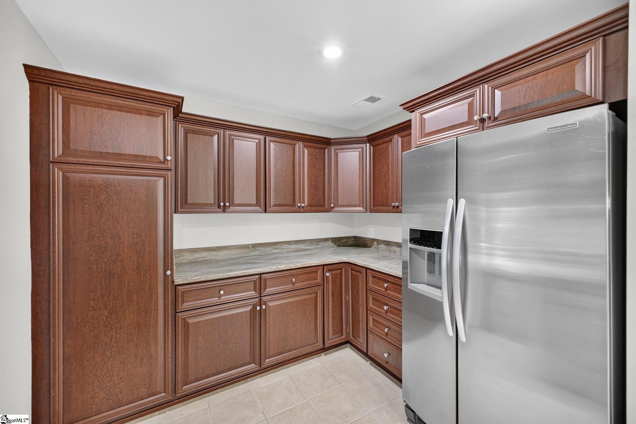 Kitchen with dark wood cabinetry, stone counters, and a stainless steel refrigerator.