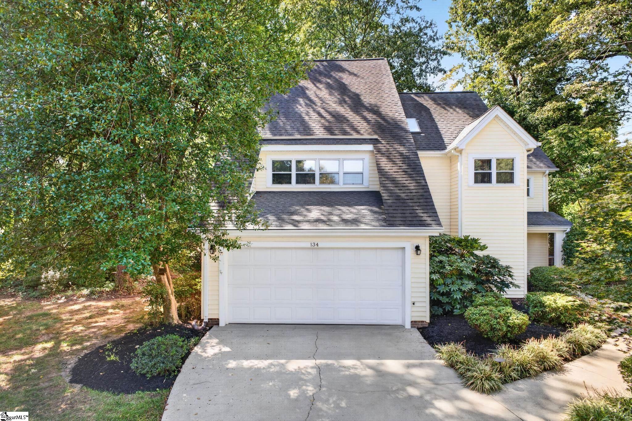 Cream multi-level house with a steep shingle roof, double garage, and mature trees.