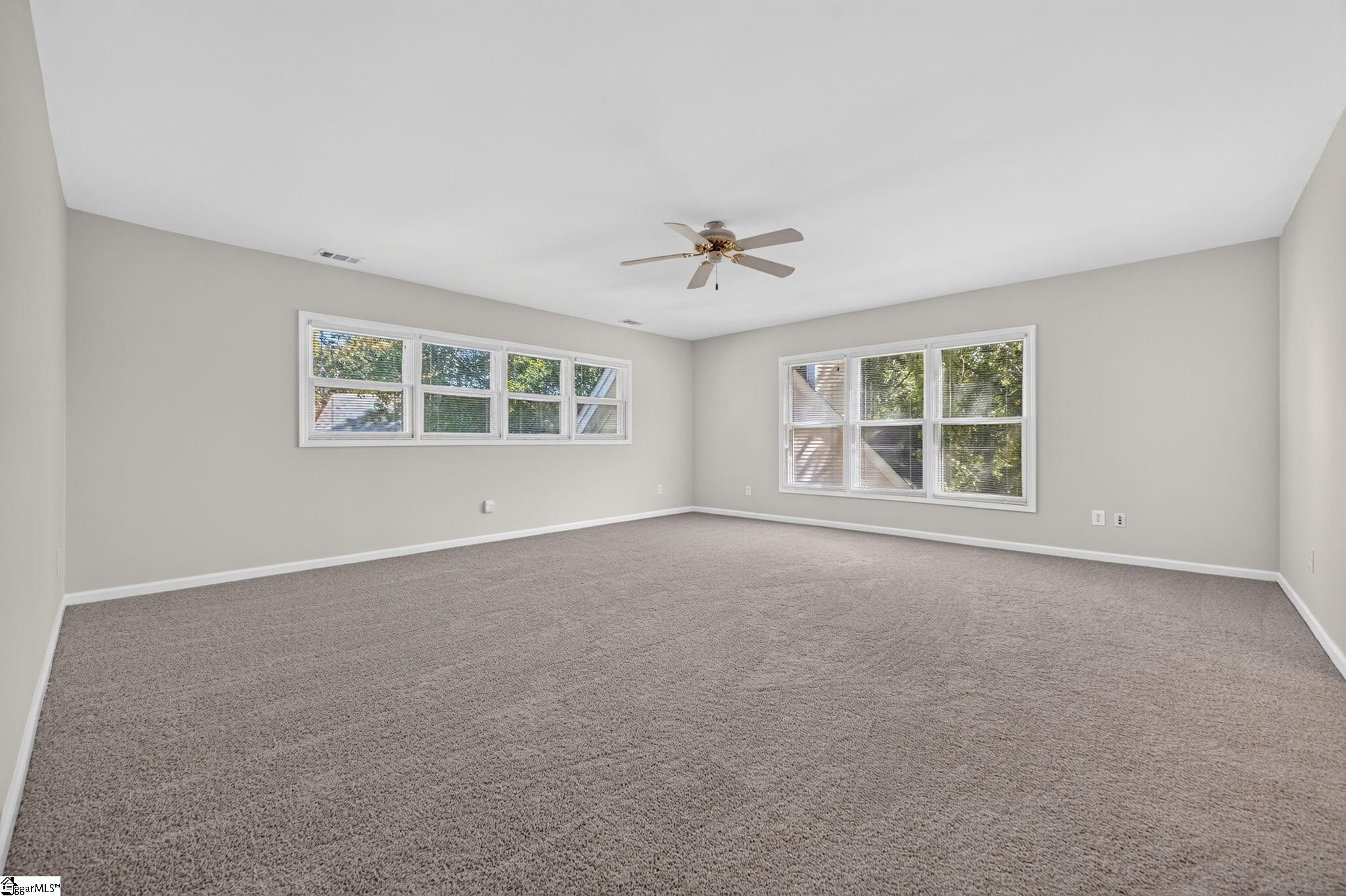 Empty carpeted room with a ceiling fan and two sets of windows.