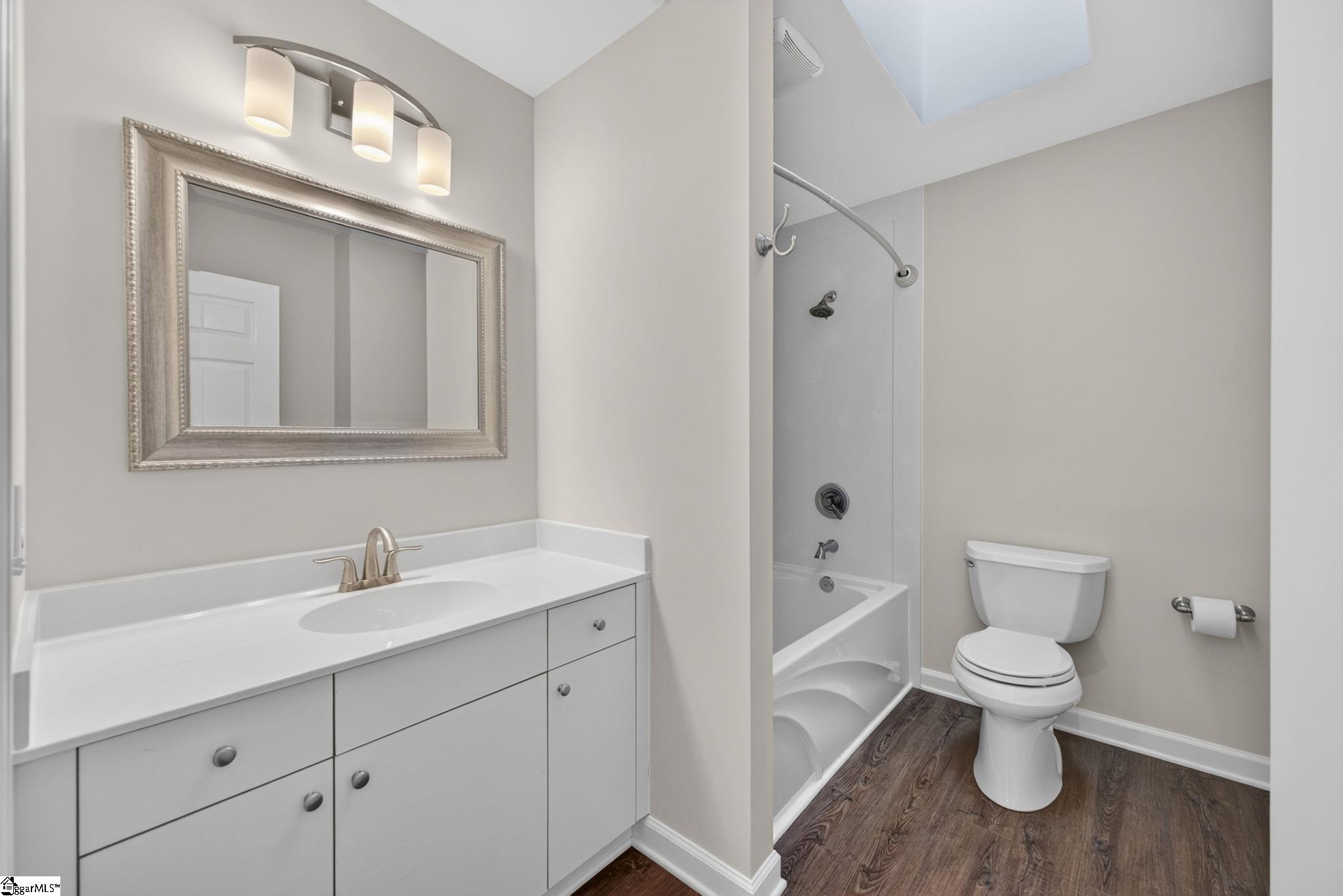 Bathroom with a white vanity, glass-enclosed tub and shower, and dark wood-look flooring.