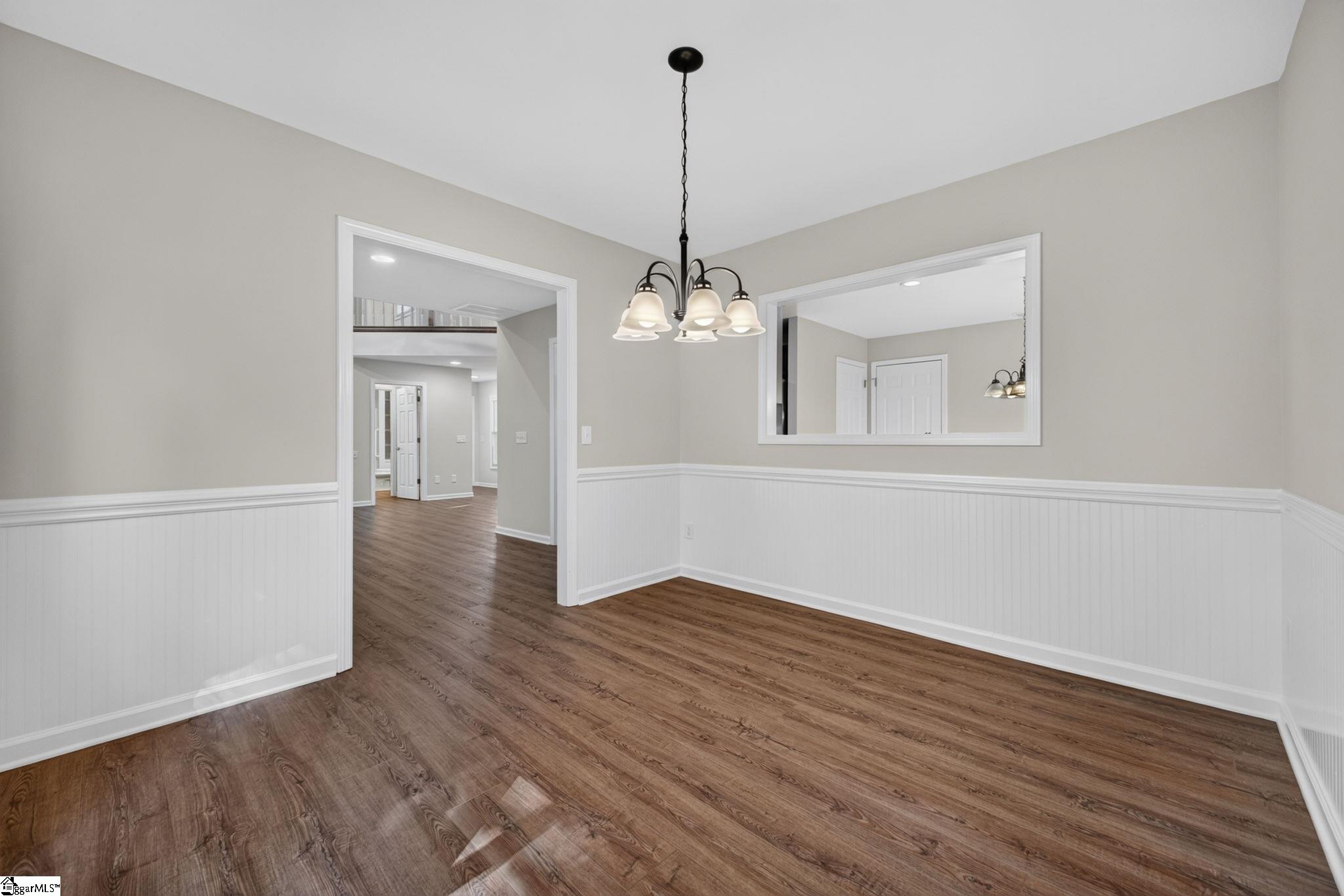 Empty dining room with wood-look floors, white wainscoting, and a multi-light chandelier.