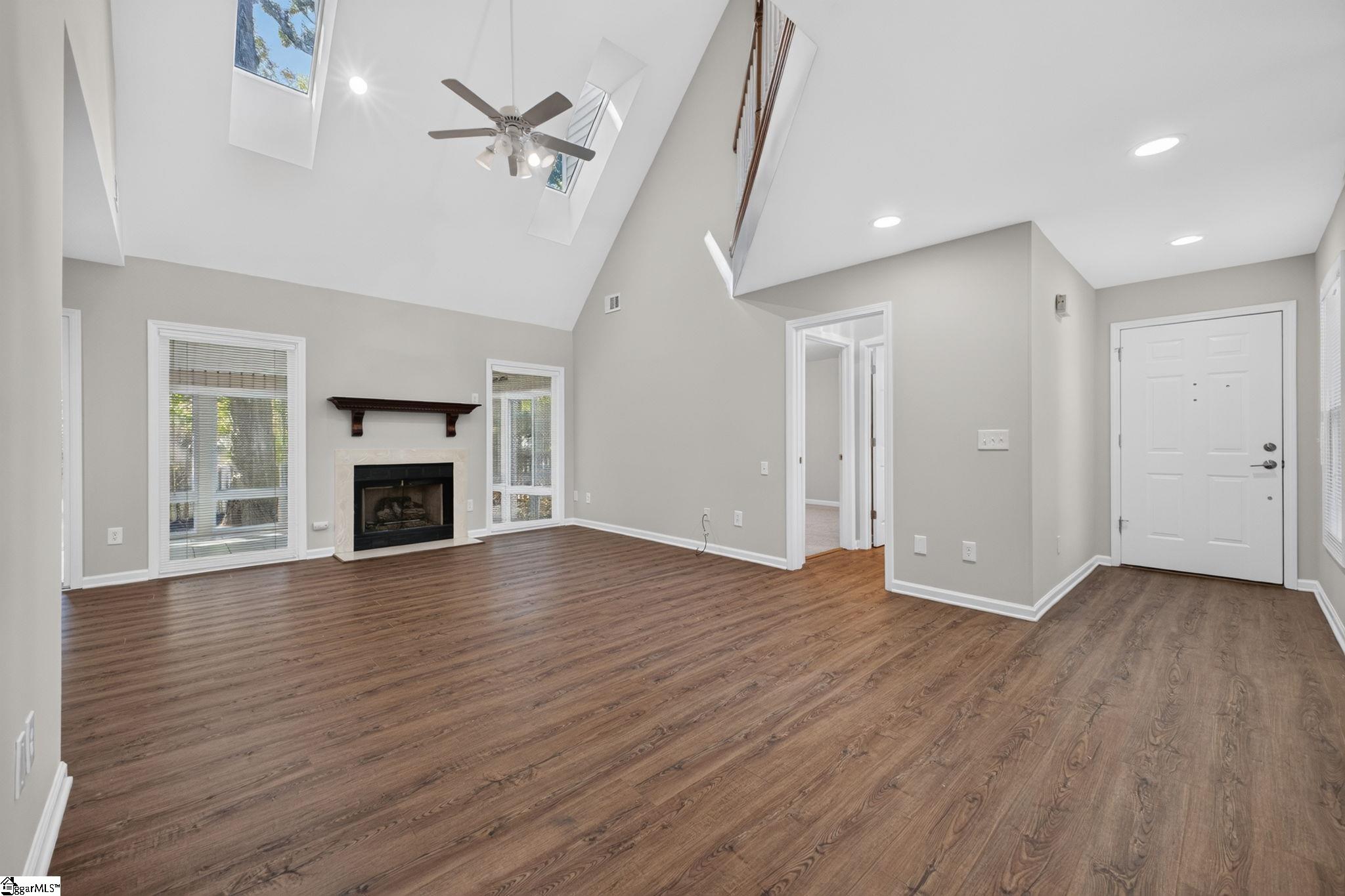 Empty living room with wood floors, a fireplace, and a vaulted ceiling with skylights.