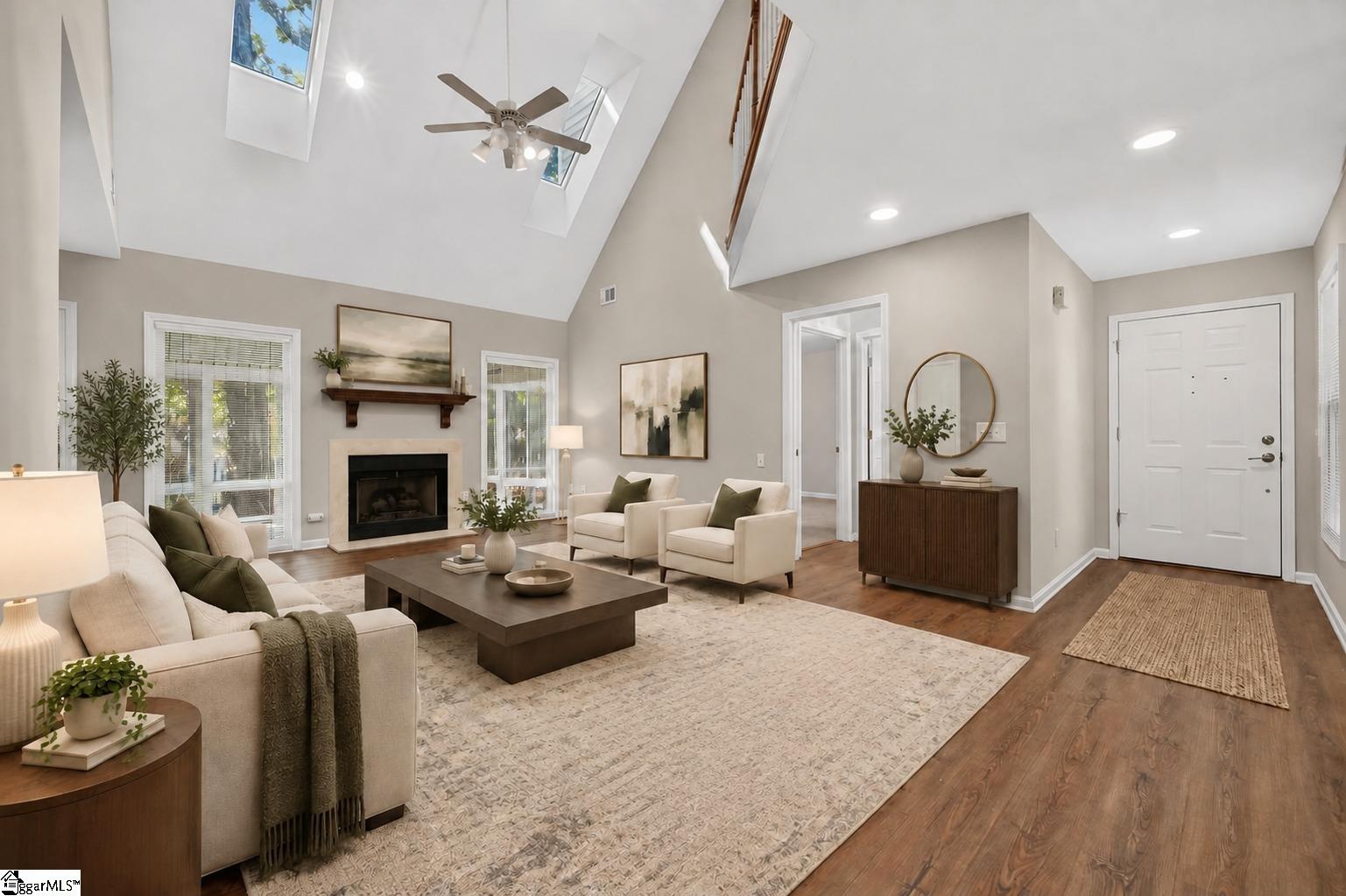 Living room with vaulted ceiling, skylights, fireplace, cream seating, and hardwood floors.