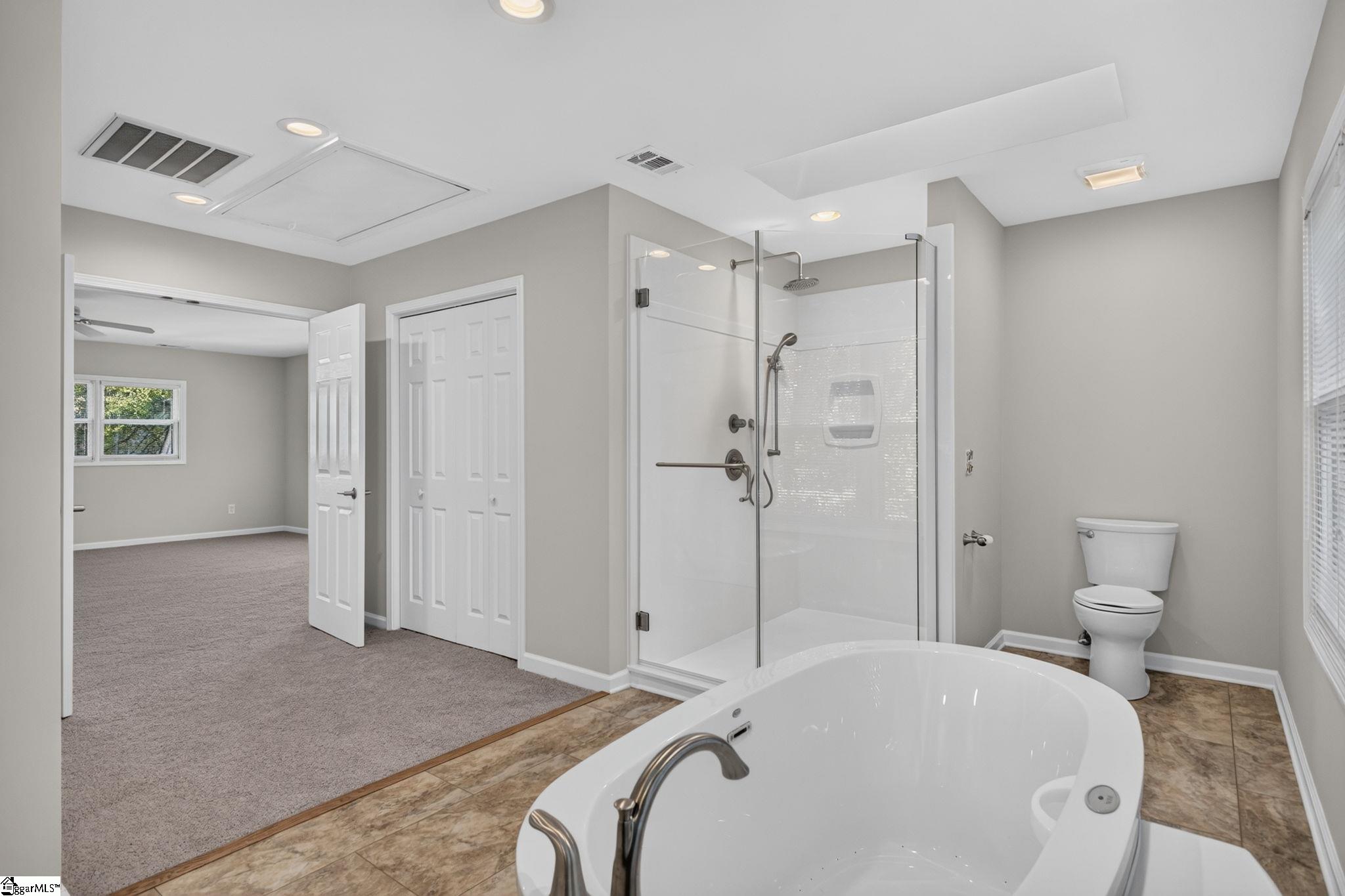 Primary bathroom with corner soaking tub, glass-enclosed shower, and adjoining carpeted room.