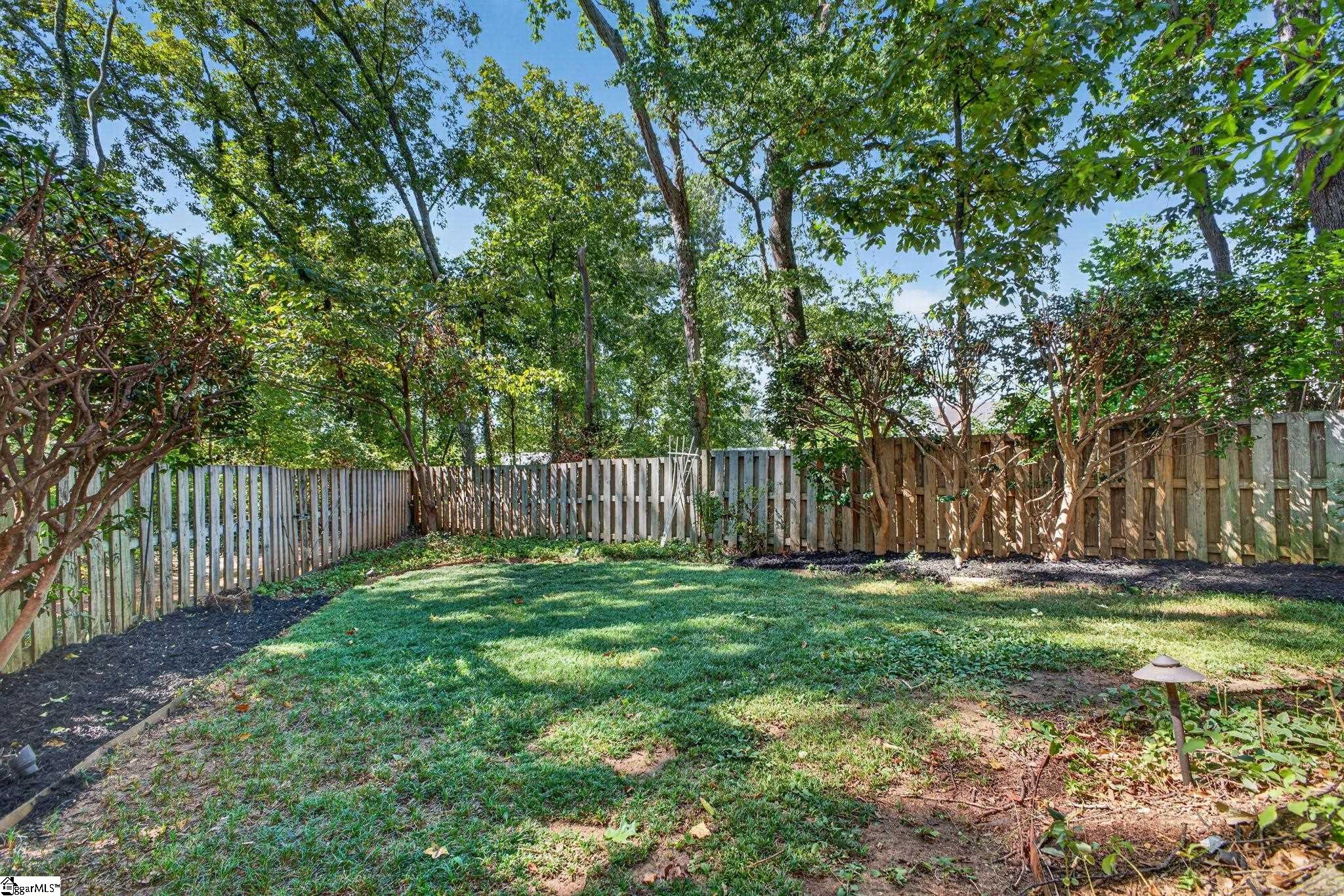 Fenced backyard with a green lawn, mature trees, and mulched planting beds.
