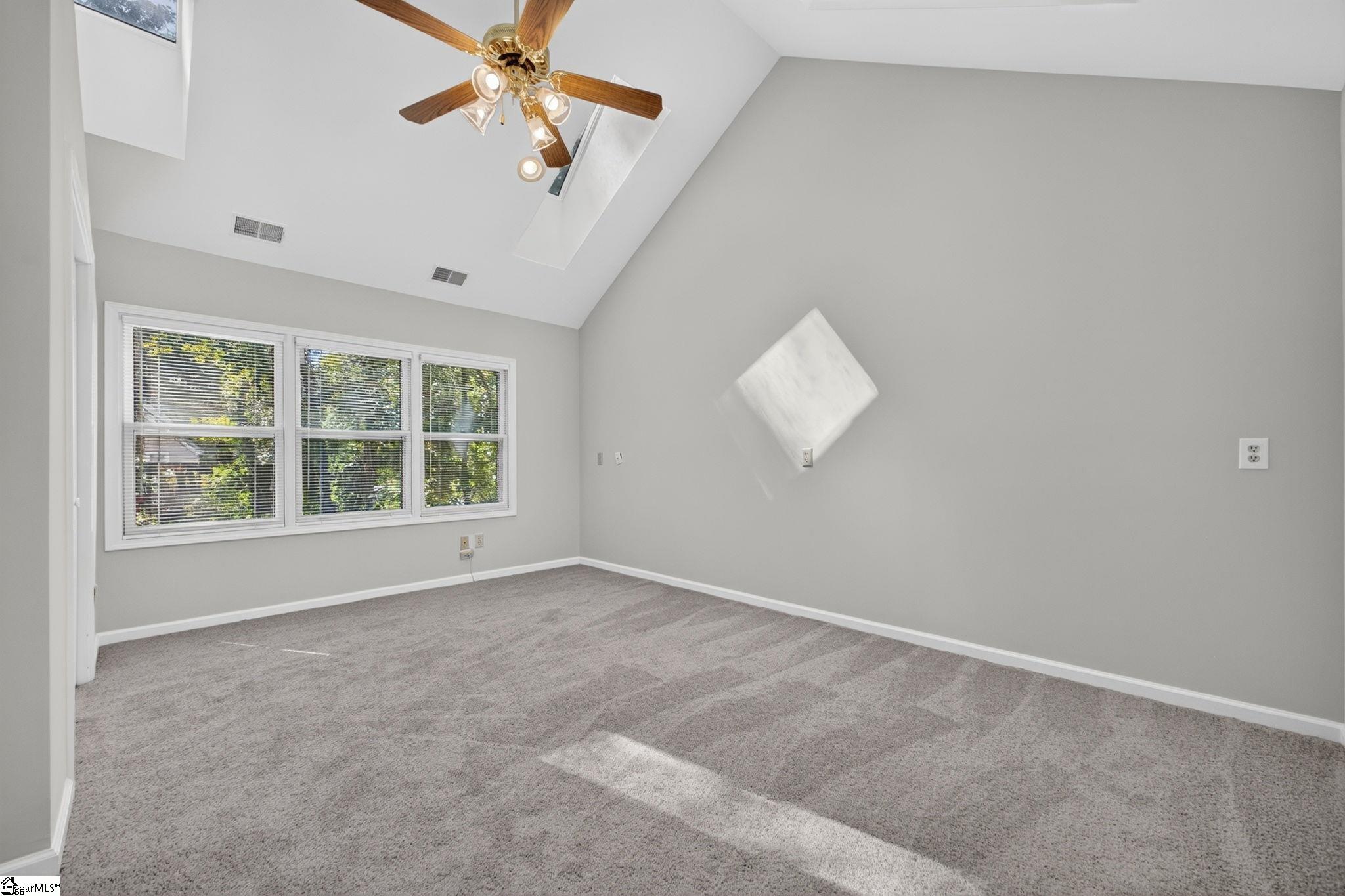 Empty carpeted bedroom with a vaulted ceiling, ceiling fan, and wide windows with blinds.