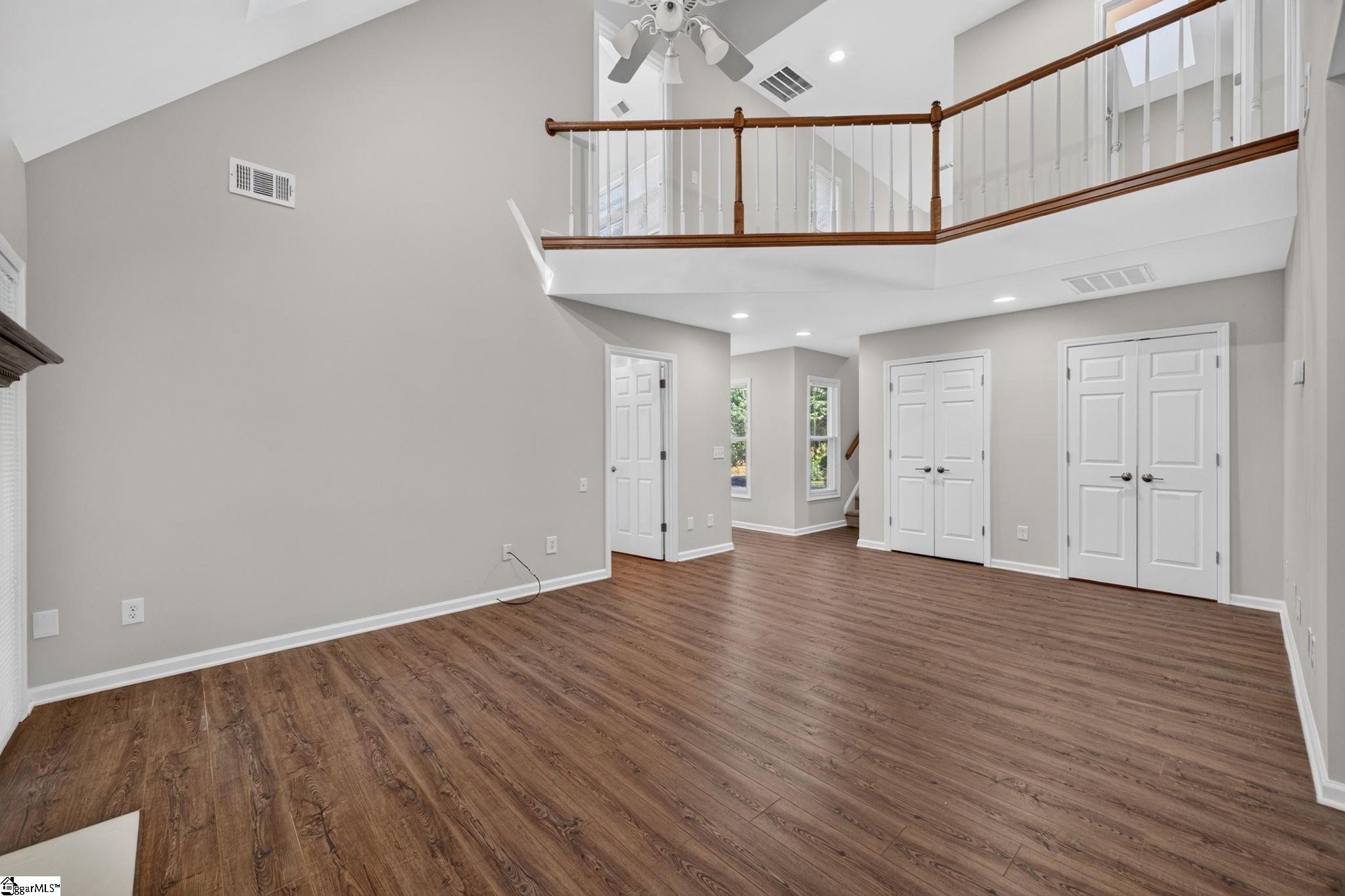 Empty two-story living area with wood-look floors and an open upper-level landing.