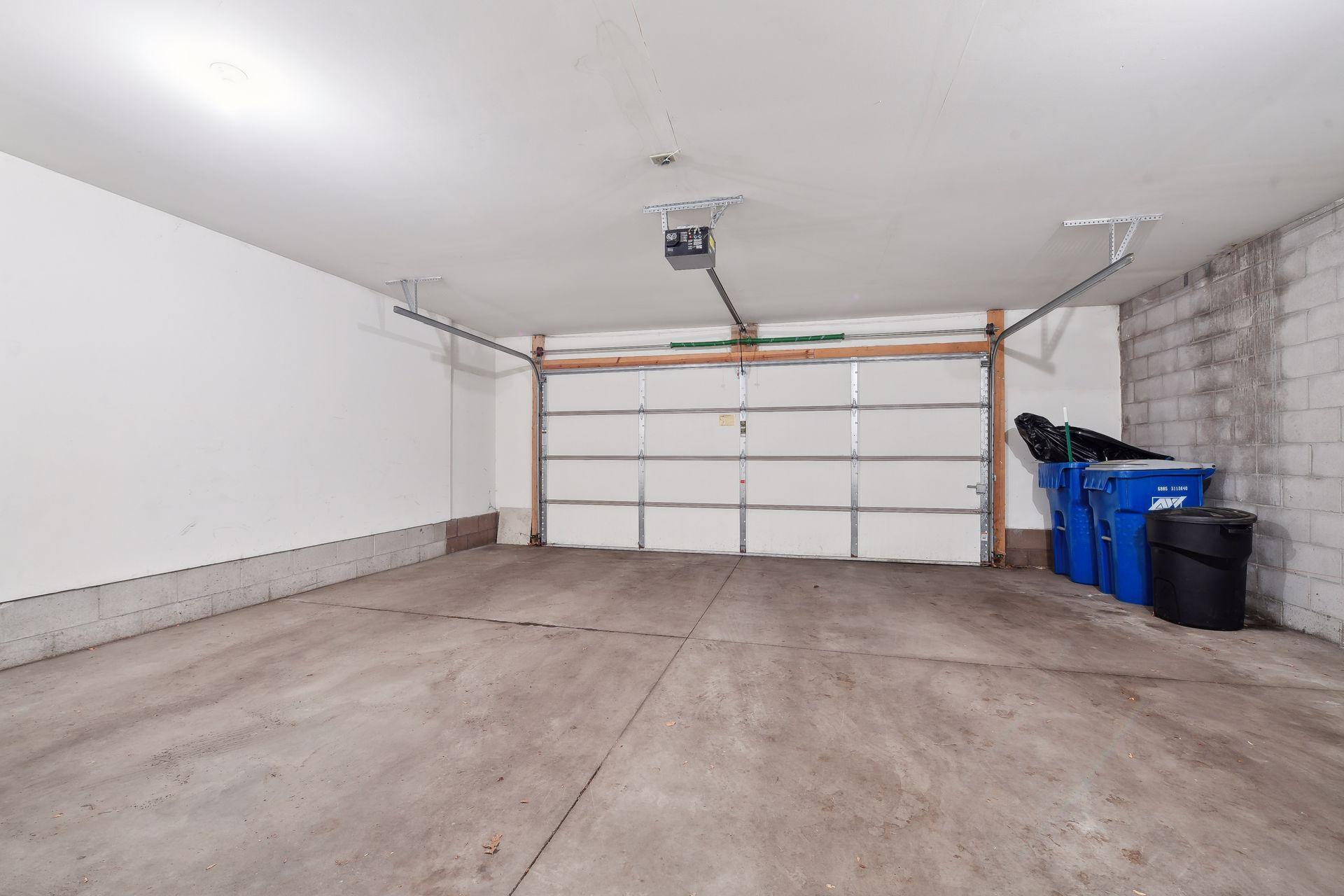 Empty garage with a closed overhead door, concrete floor, and blue bins along the block wall.