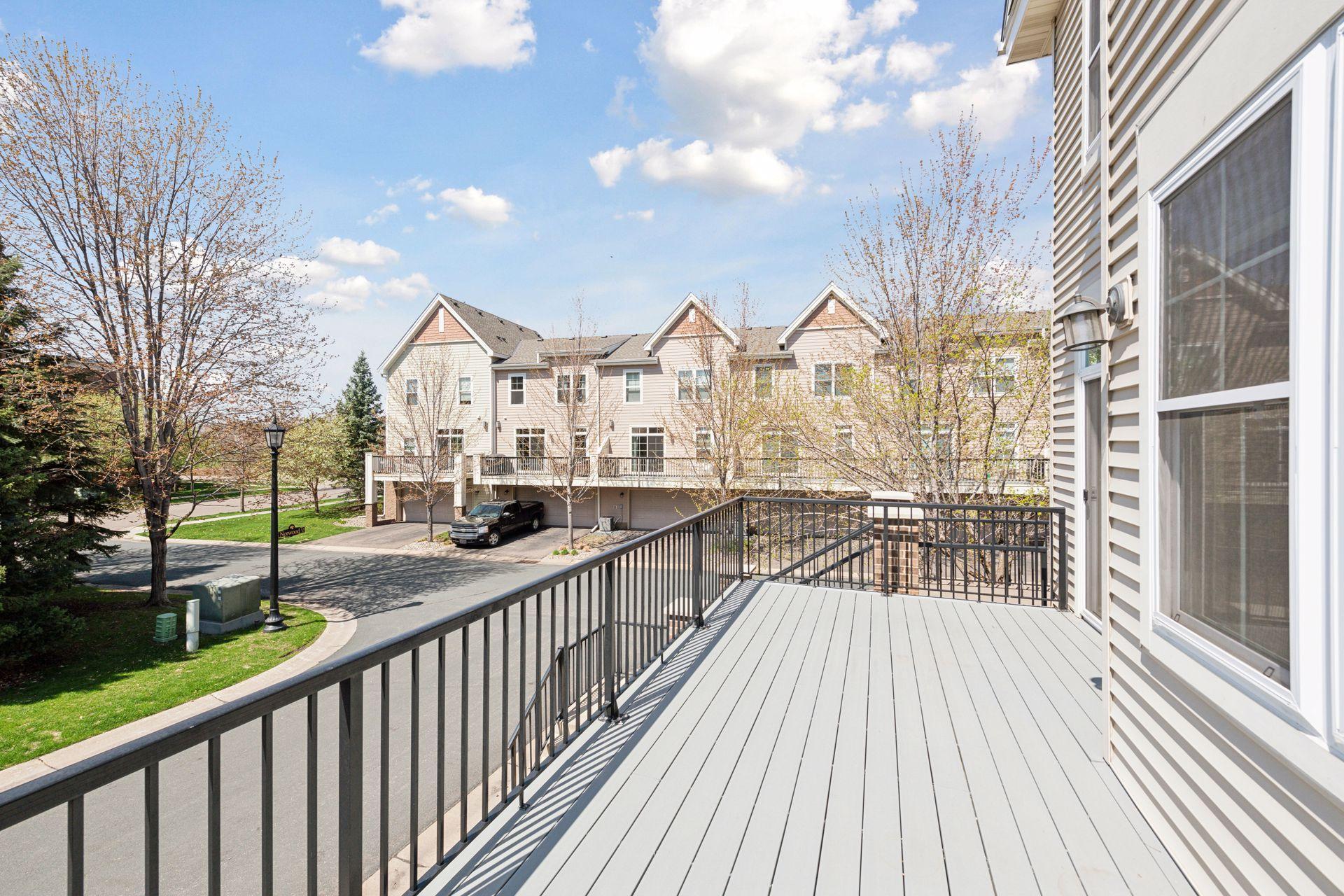 Wide gray deck with black railings overlooking neighboring townhouses and a tree-lined residential street.