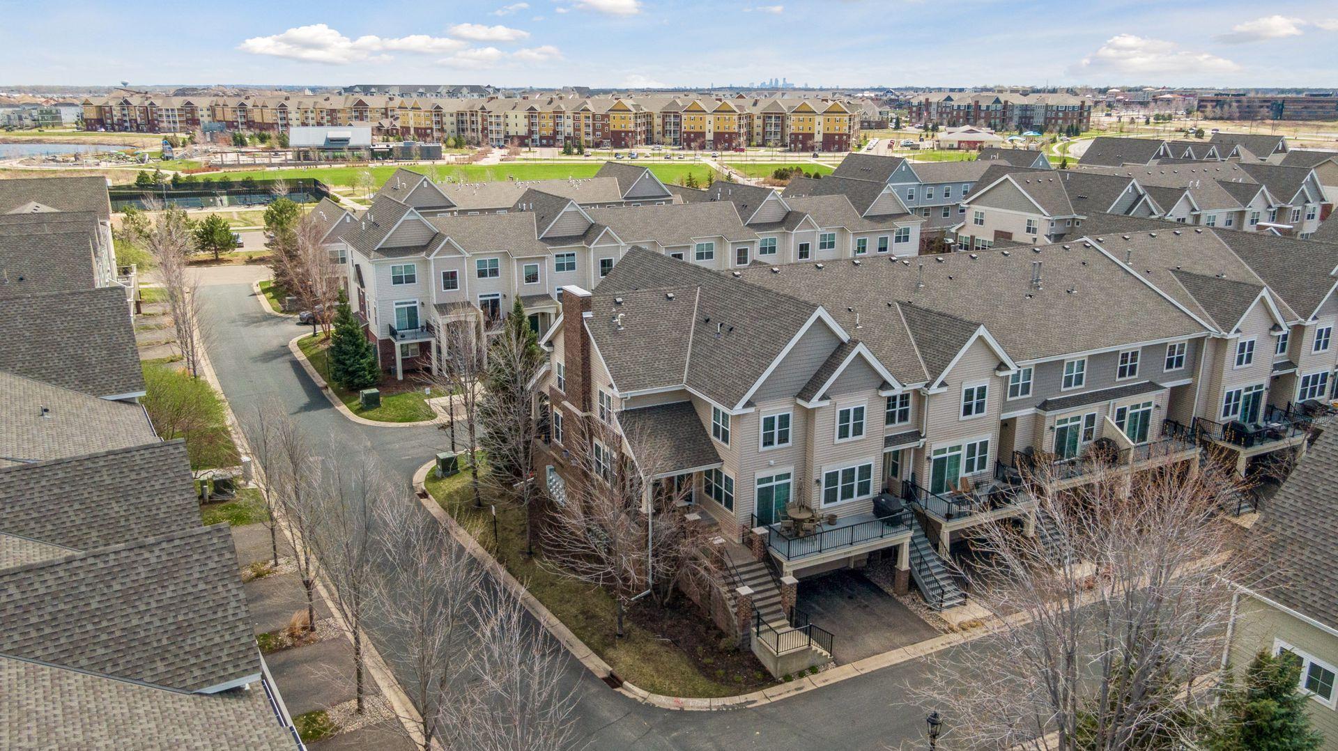 Aerial view of attached townhomes along a curving street, with a distant city skyline.