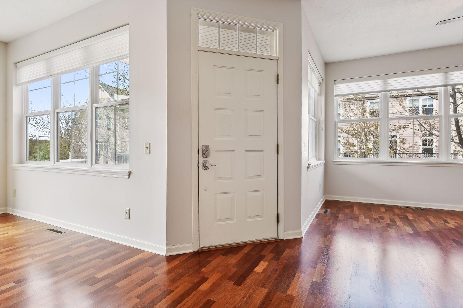 Empty entryway with a paneled front door, tall windows, and polished hardwood floors.