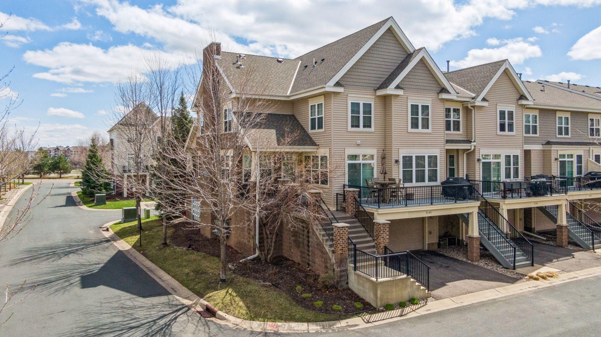Beige townhouse with steep gabled roofs, a raised deck, and exterior stairs on a residential corner.