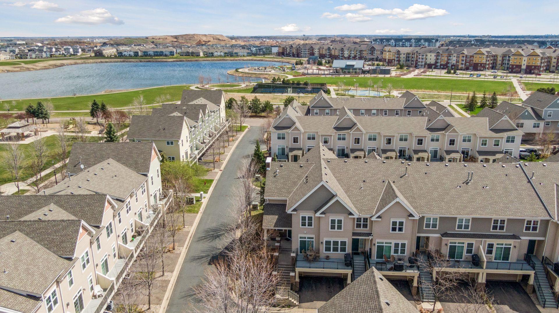 Aerial view of attached townhomes beside a lake and landscaped walking paths.