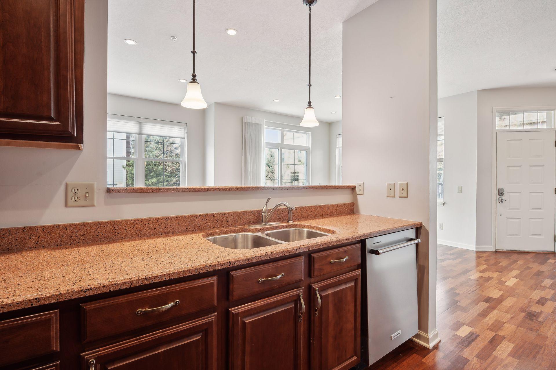 Kitchen with dark wood cabinets, speckled countertops, a double sink, and a stainless steel dishwasher.