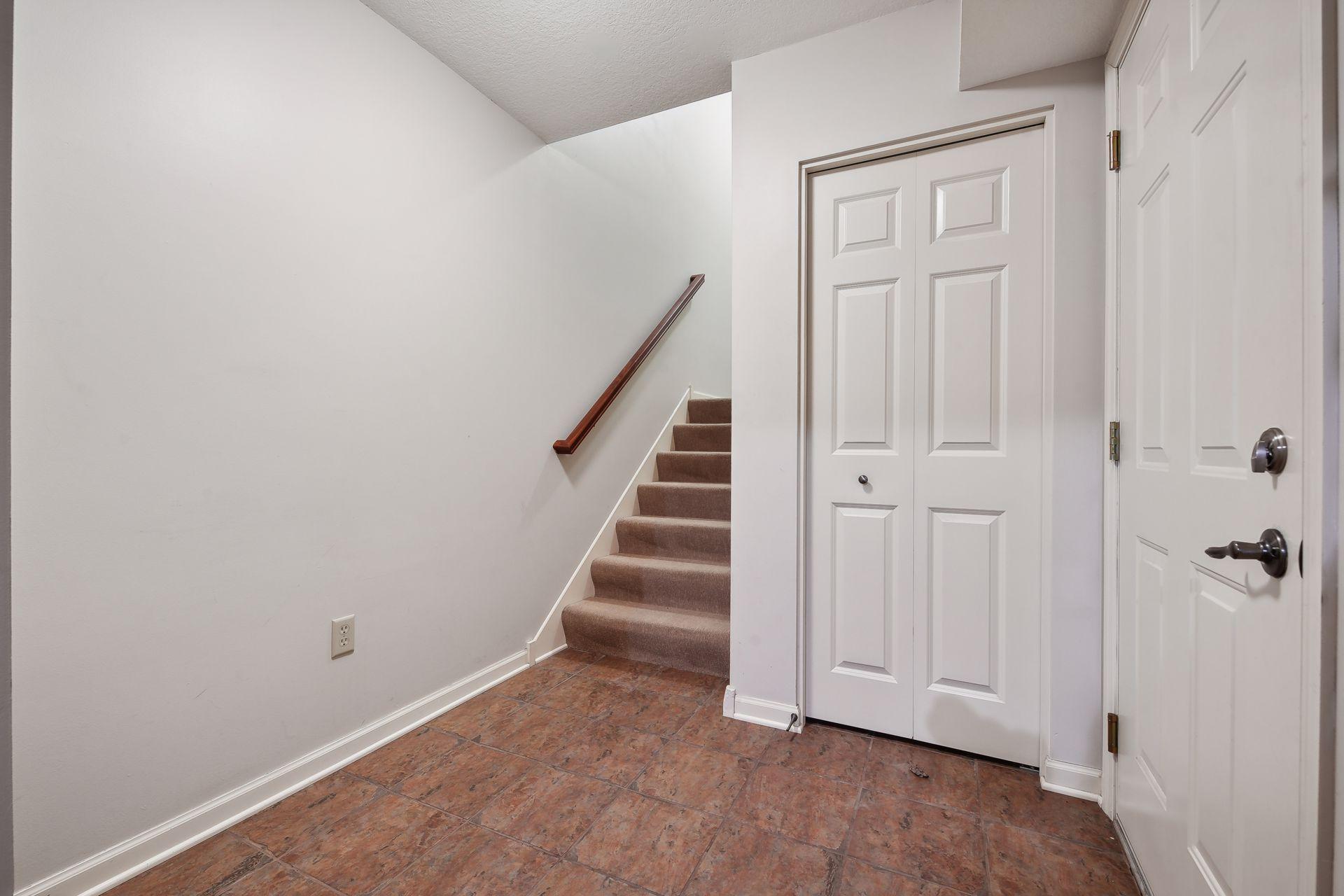 Entry hall with tiled floor, carpeted stairs, and white paneled doors.