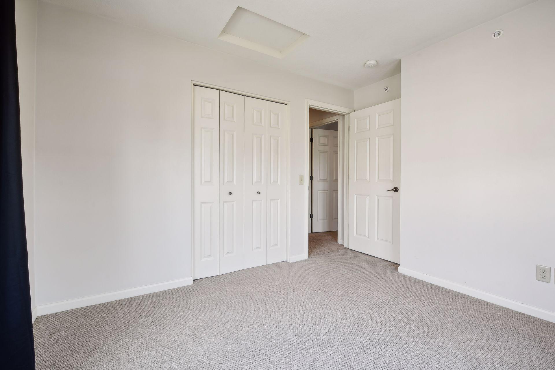 Empty carpeted bedroom with a white built-in closet and open doorway.