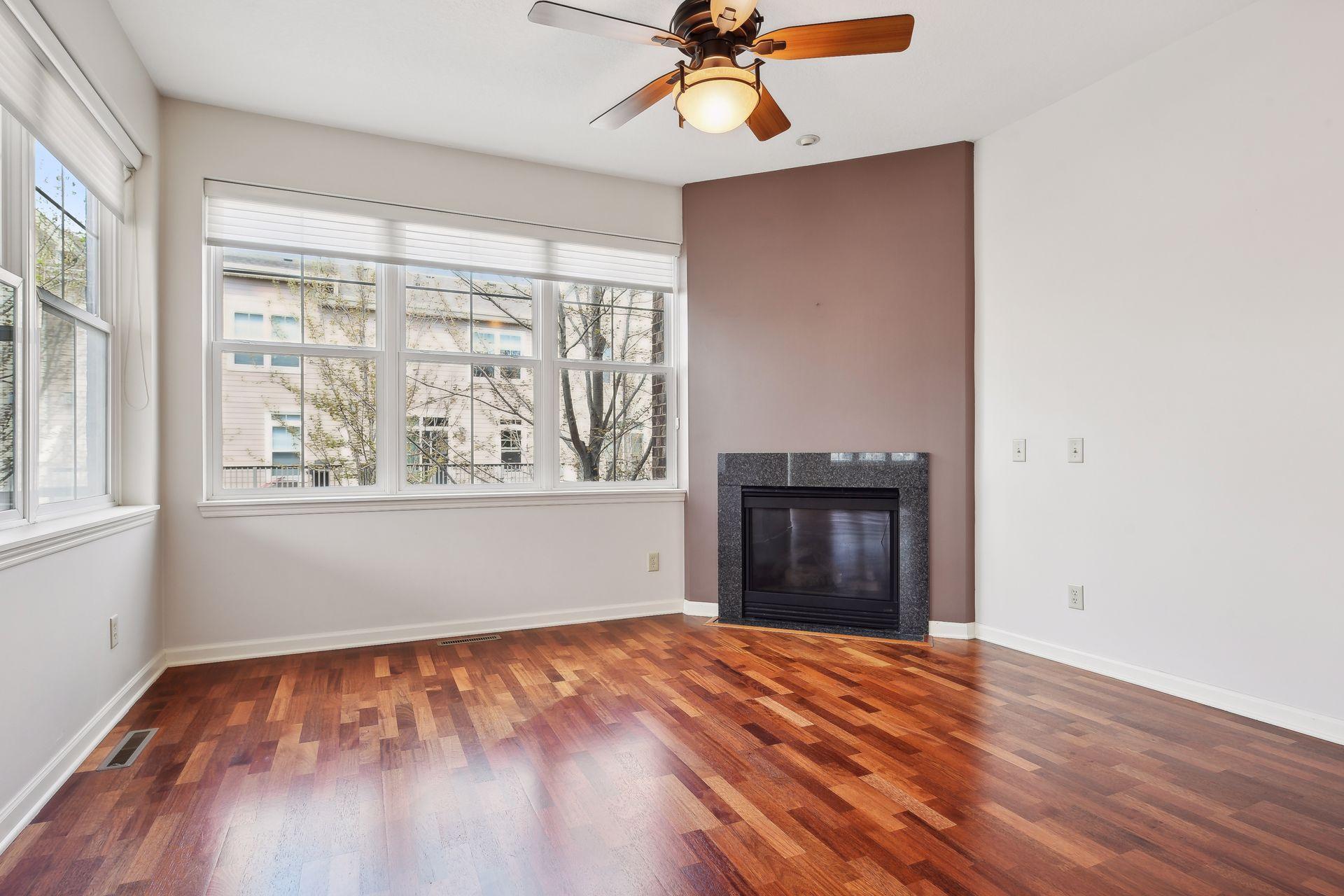 Unfurnished living room with hardwood floors, large windows, and a fireplace on a mauve accent wall.