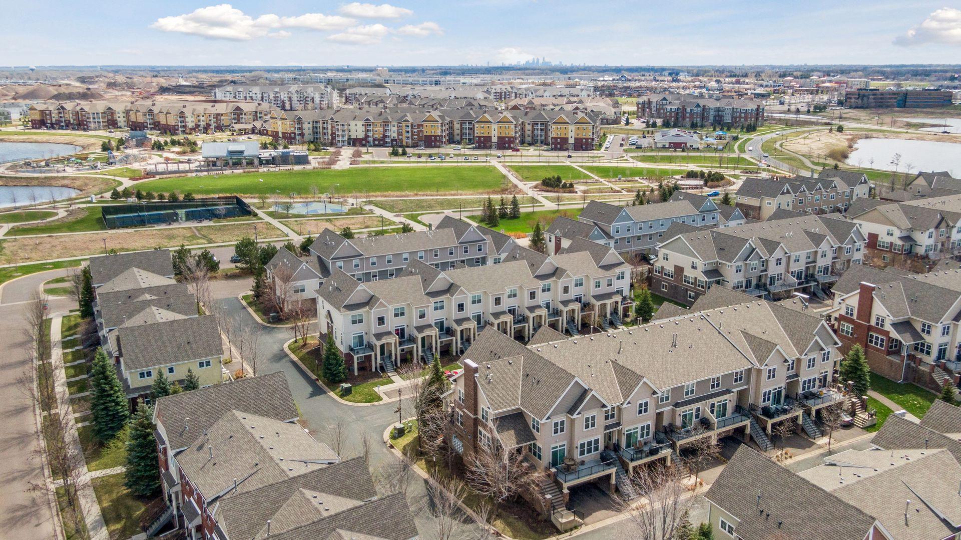 Aerial view of a townhouse neighborhood with parkland, ponds, and a distant city skyline.