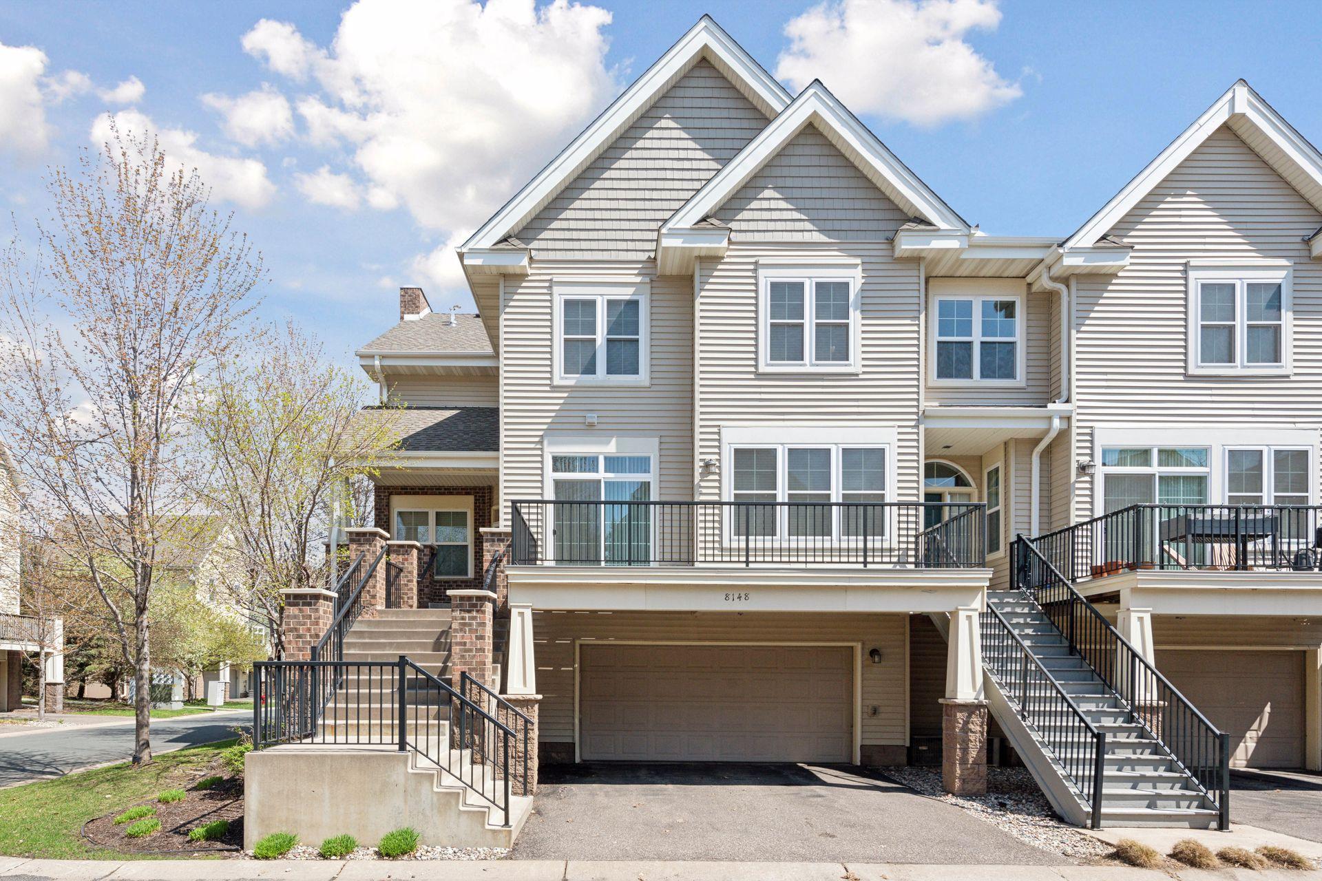Beige townhouse exterior with steep gables, black-railed stairs, and garage marked 8148.