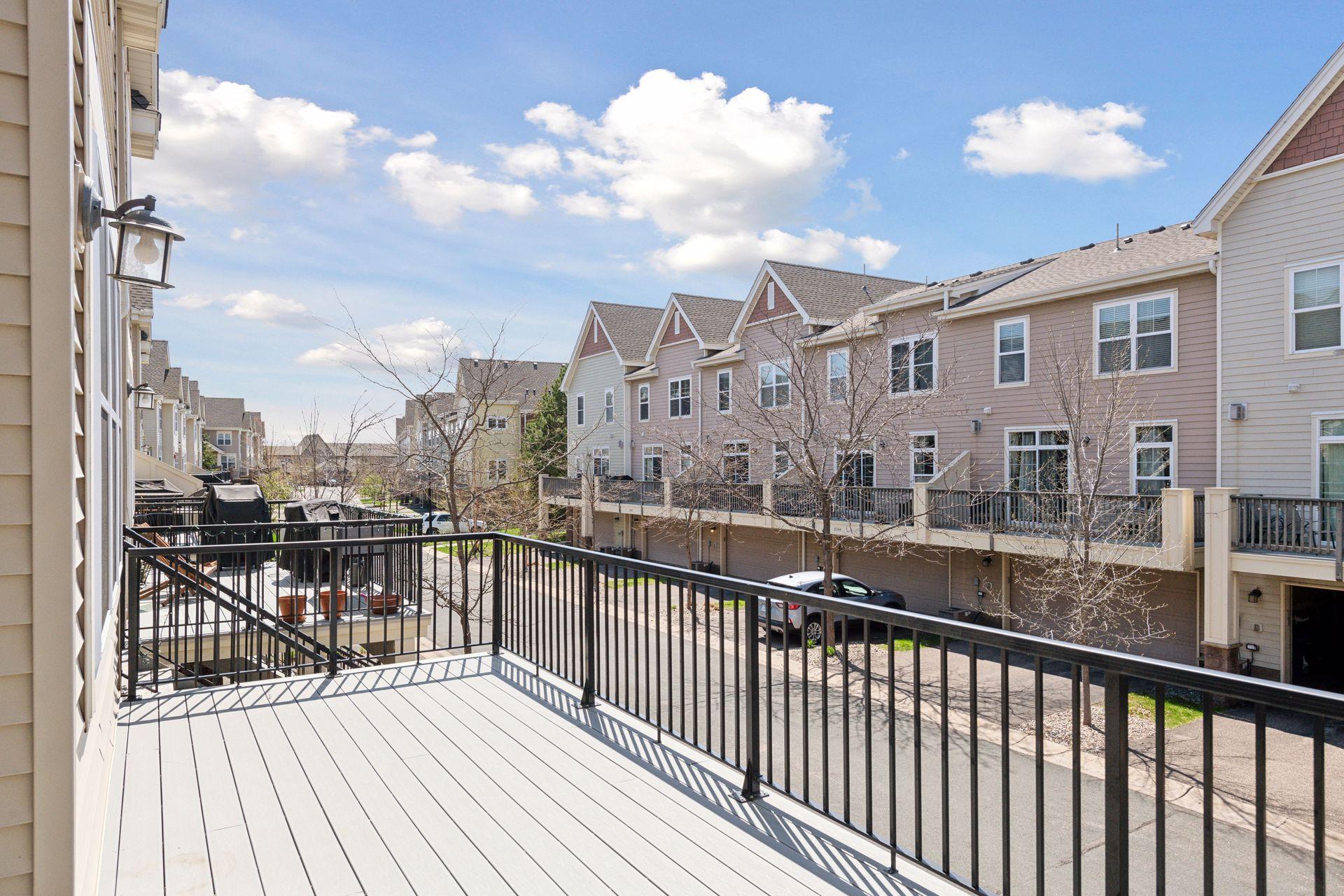 Raised deck with black railings overlooks neighboring townhomes and a shared lane.