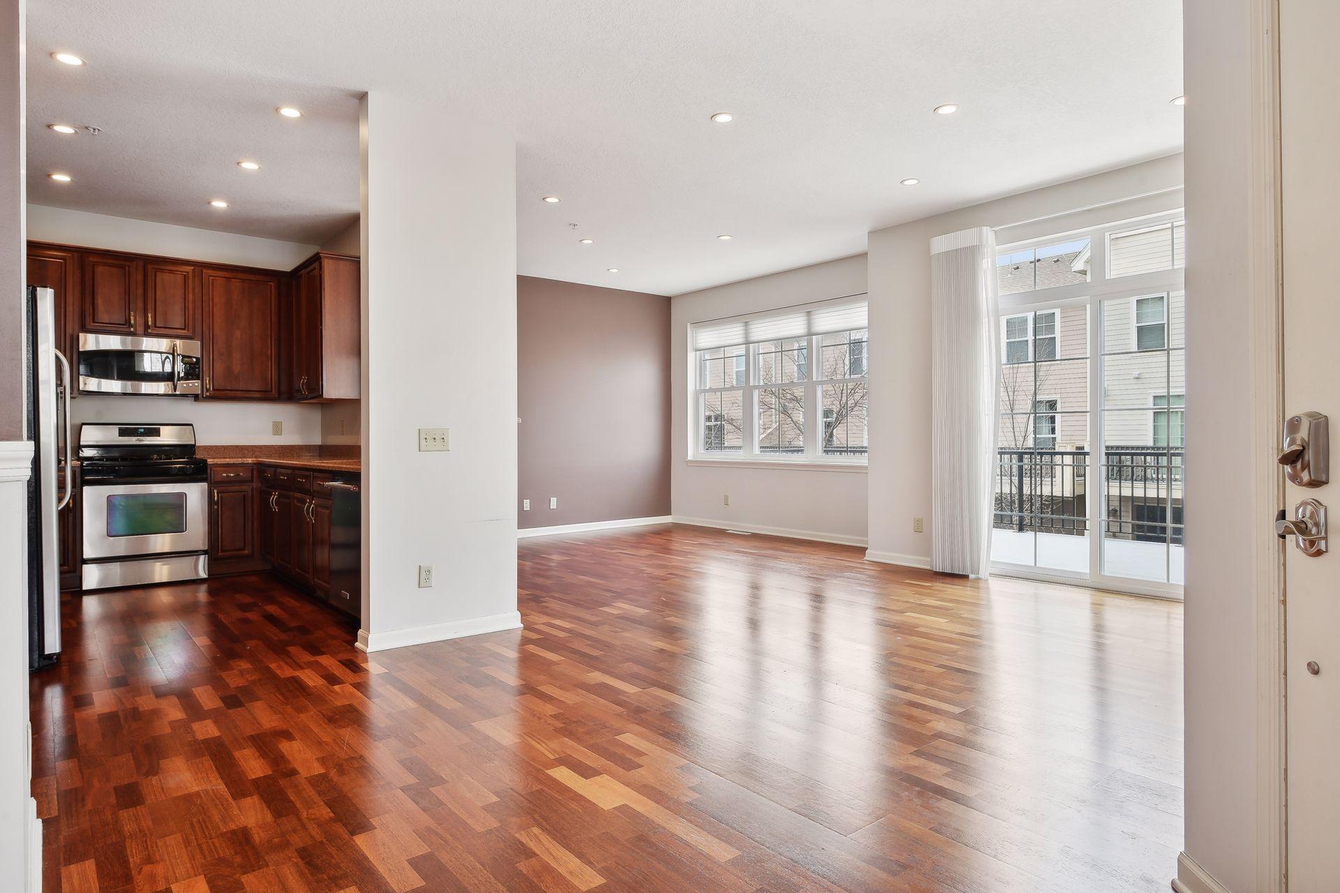 Vacant kitchen and living area with cherry cabinets, hardwood floors, and a balcony-facing sliding glass door.