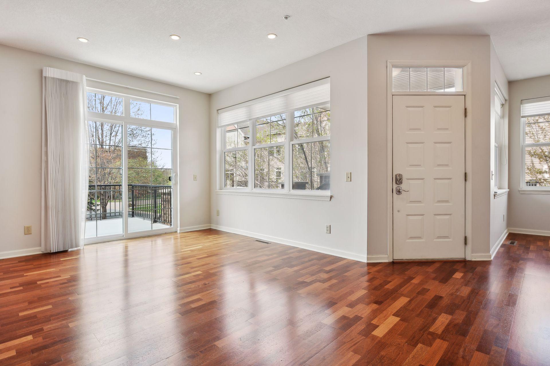 Vacant living room with reddish hardwood floors, large windows, and a glass door to the balcony.