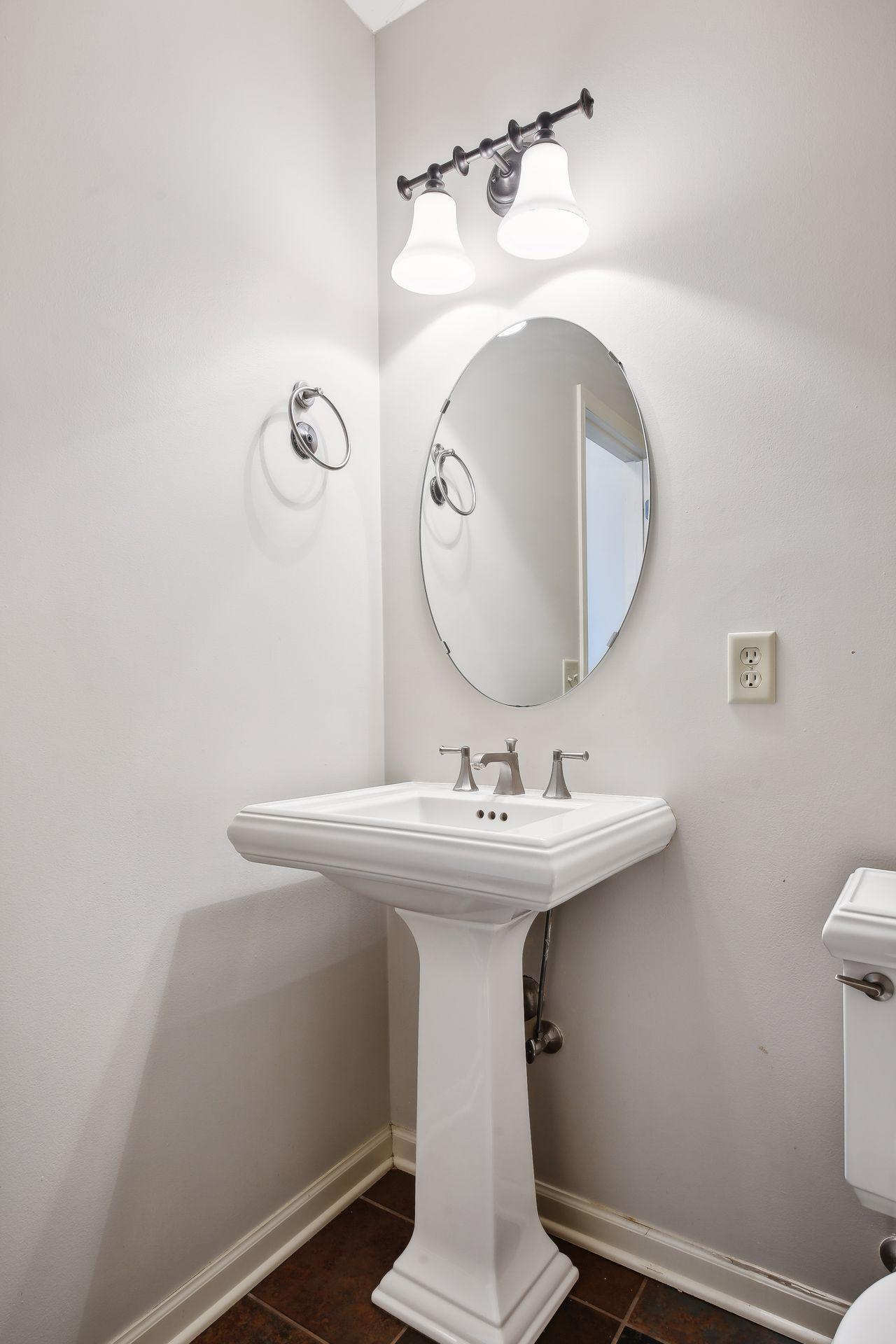 Bathroom with a white pedestal sink, oval mirror, and chrome two-light fixture.