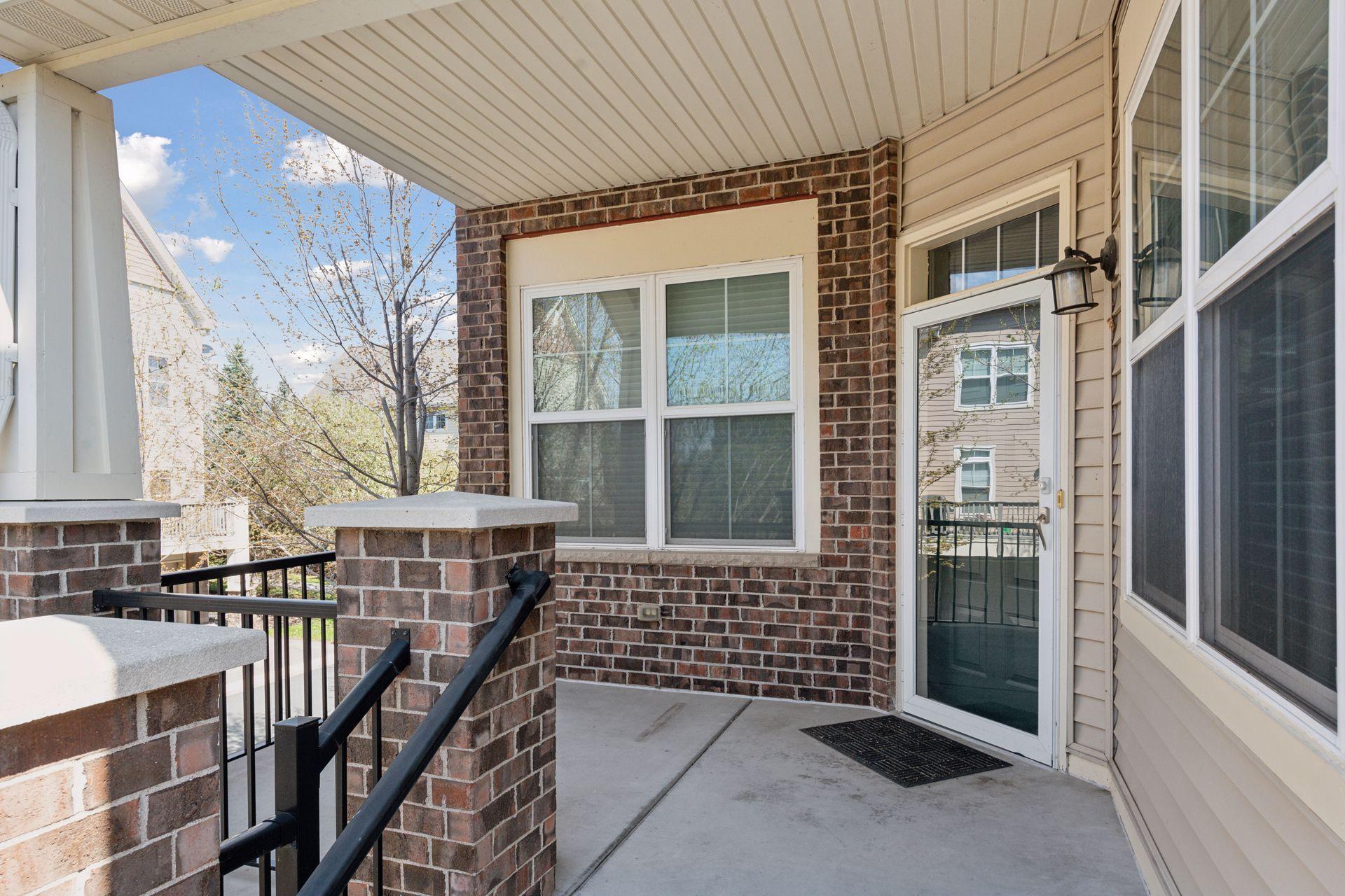 Covered porch with brick columns, black railing, and a glass door.