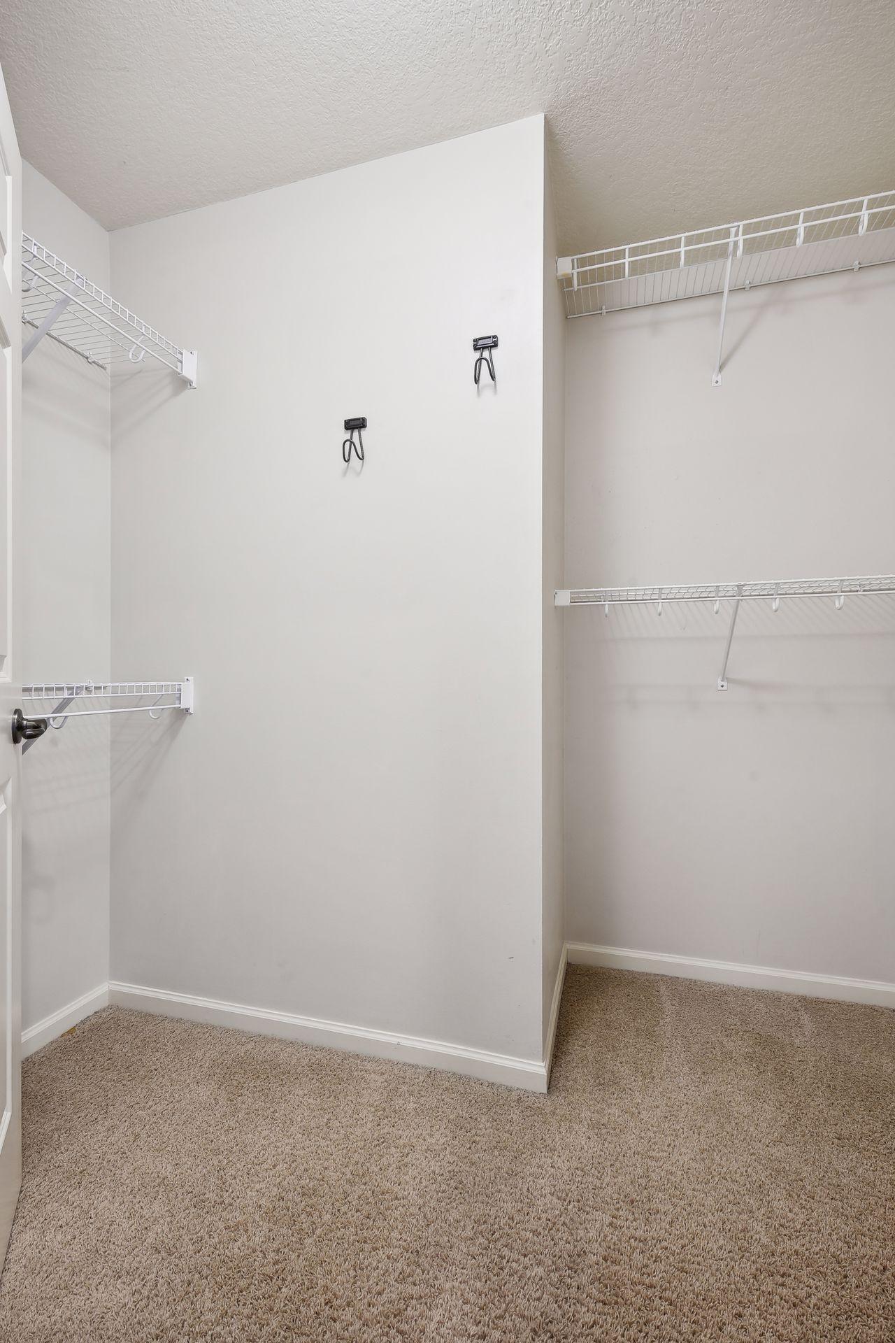 Walk-in closet with white wire shelving and beige carpeting.