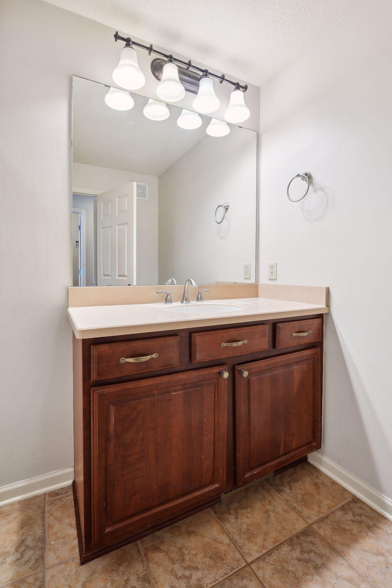 Bathroom vanity with dark wood cabinetry, a large mirror, and tan tile flooring.