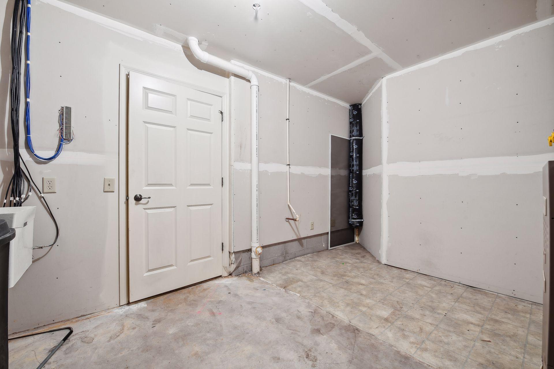 Unfinished utility room with exposed wiring, plumbing pipes, and a white paneled door.