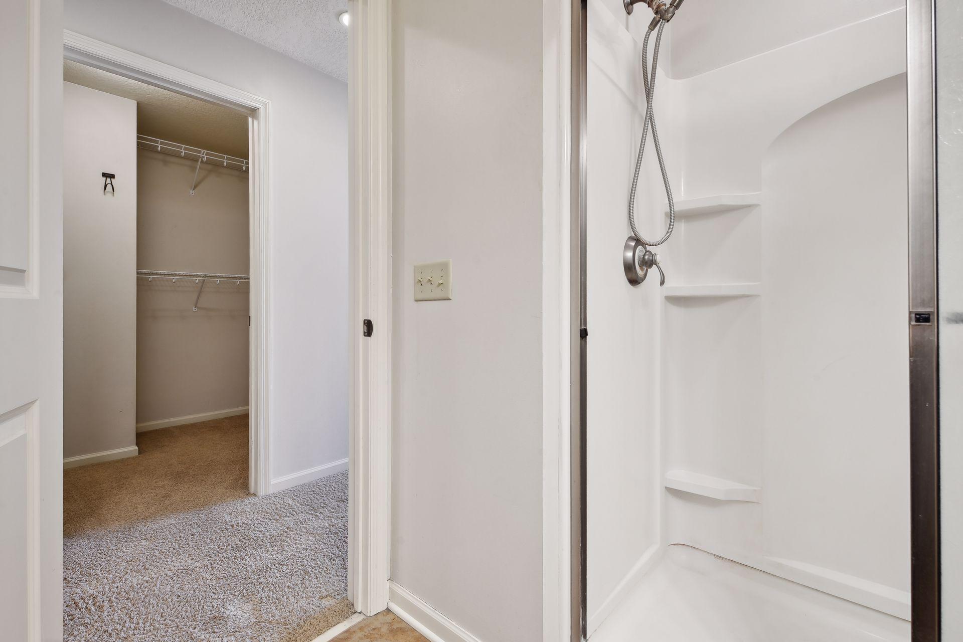 White shower stall with built-in shelves beside an open, carpeted walk-in closet.