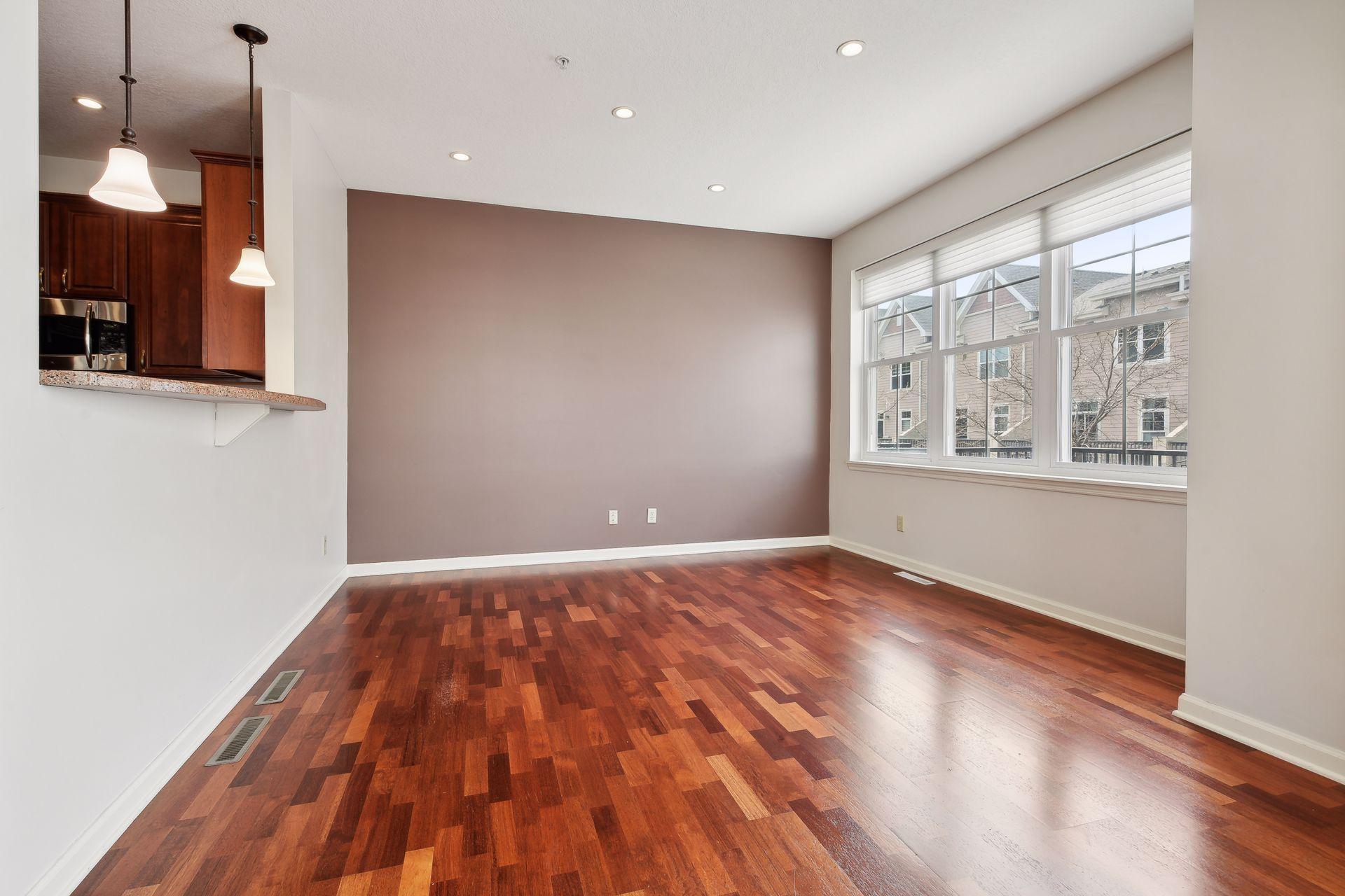 Empty dining area with reddish hardwood floors, large windows, and a pass-through to the kitchen.